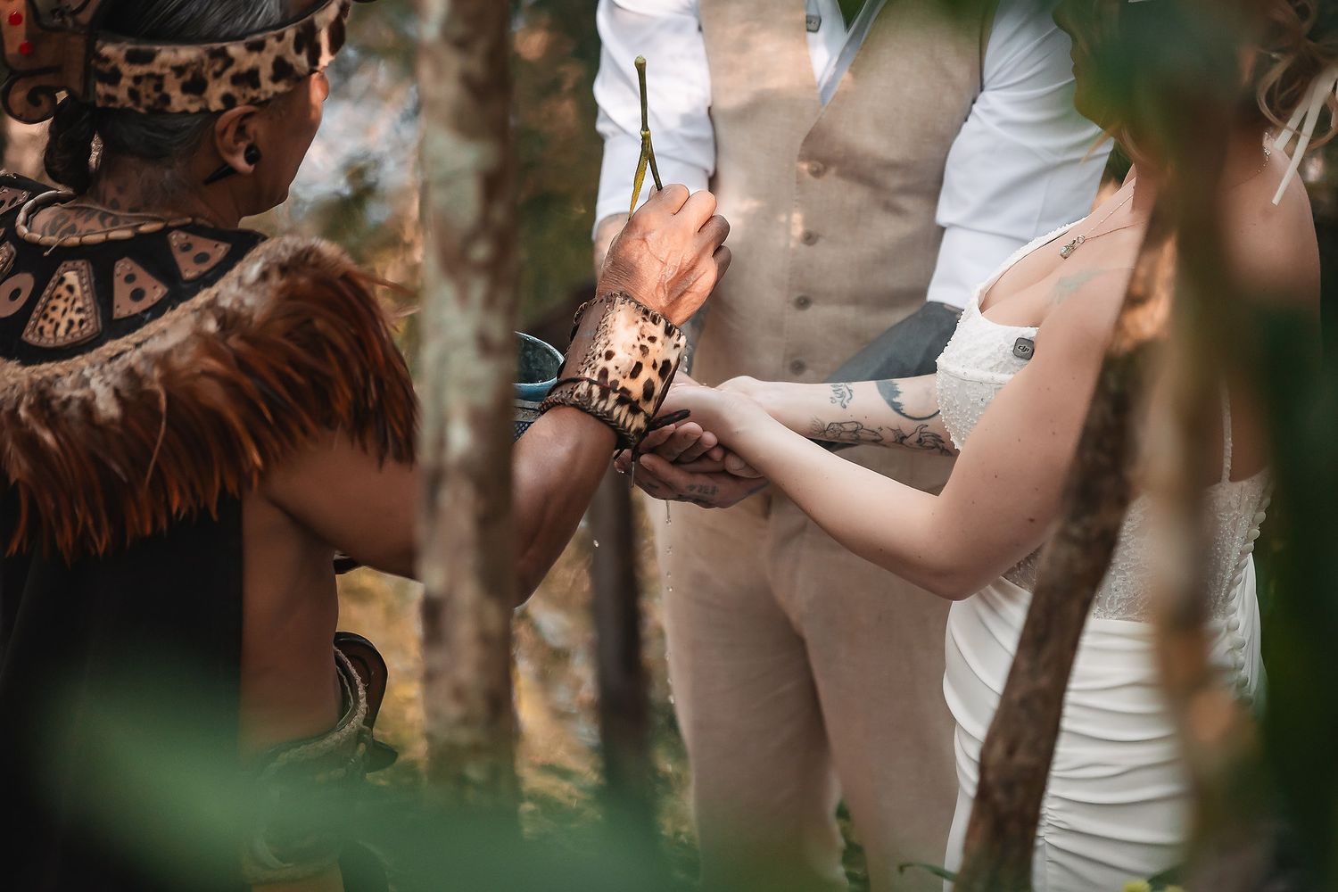 A shaman performing a traditional handfasting ceremony outdoors, tying a leopard-print cord around a couple's wrists.