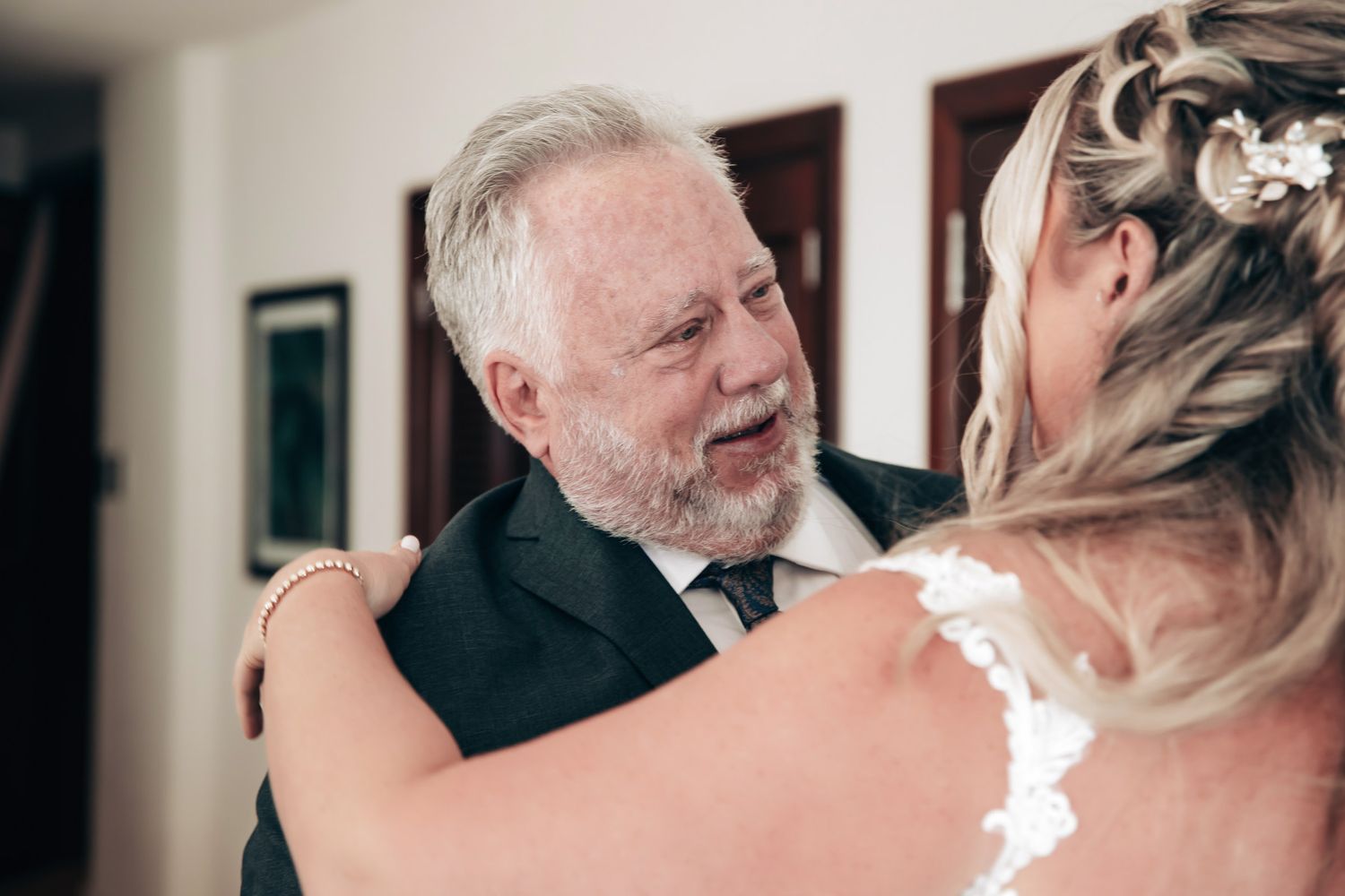 An emotional father with a white beard embraces his daughter in a wedding dress during a heartfelt first look moment.