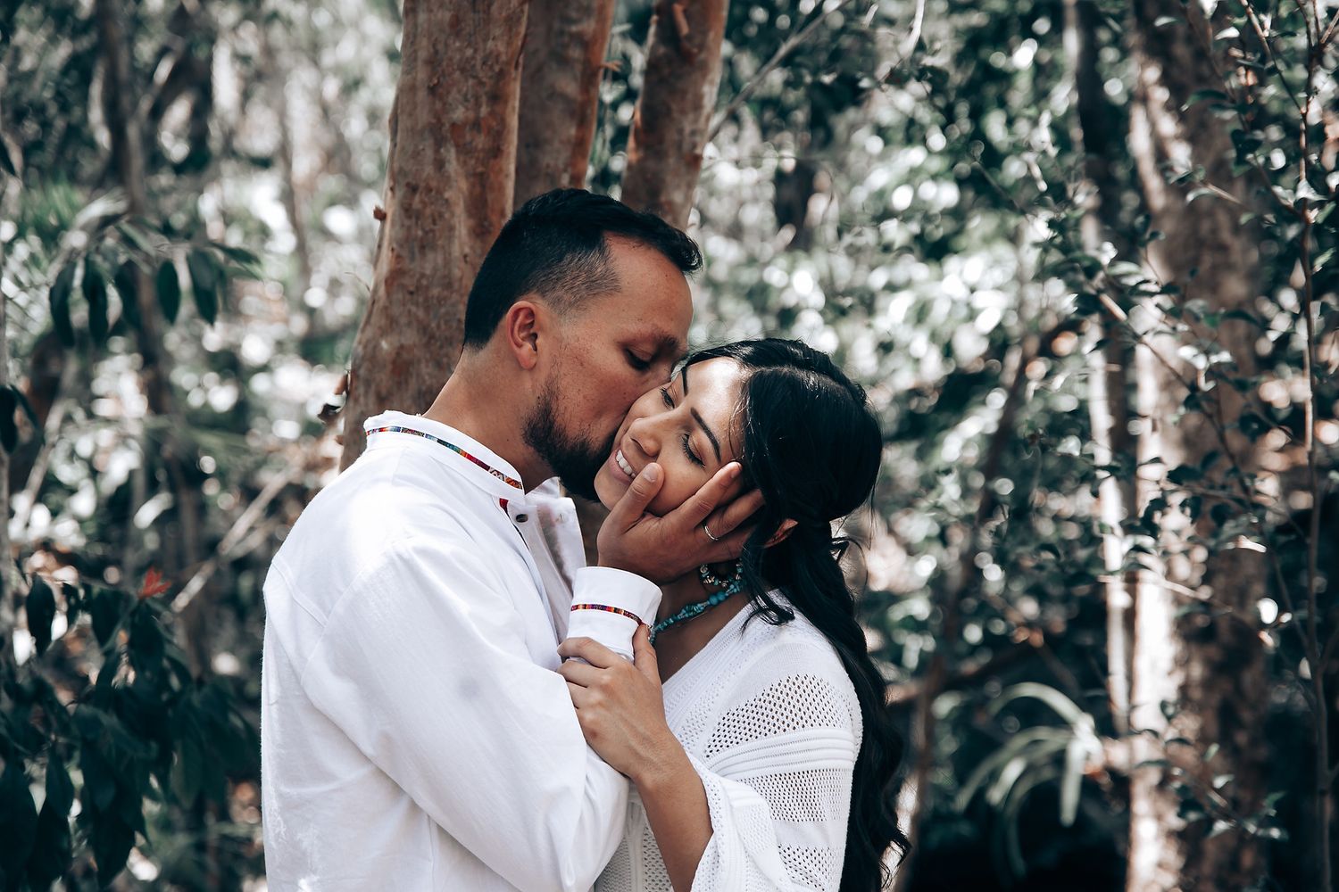 Intimate wedding moment between couple in white clothing in a forest setting.