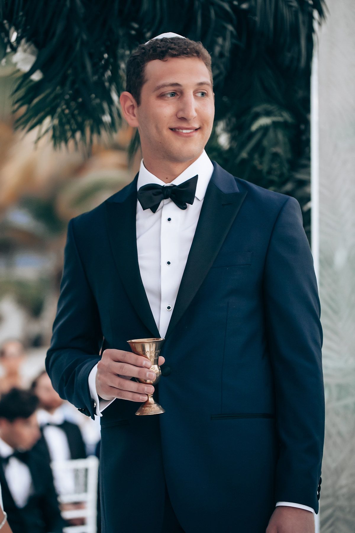 Person in black tuxedo holding cocktail glass at formal event.
