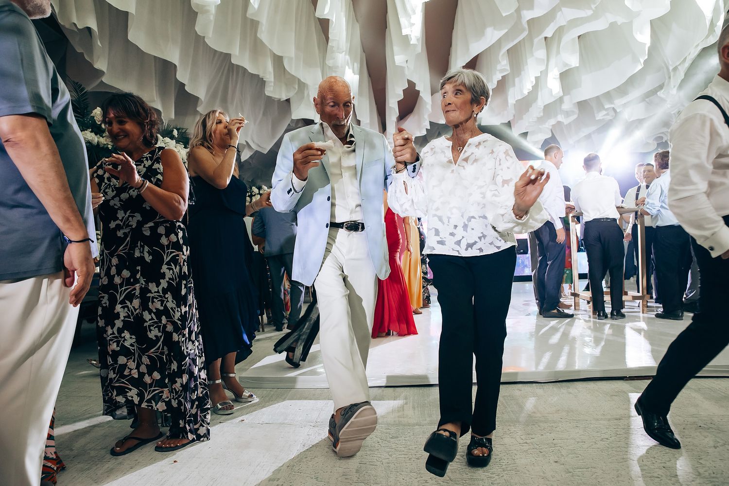 Wedding celebration with guests dancing under hanging white fabric decorations.