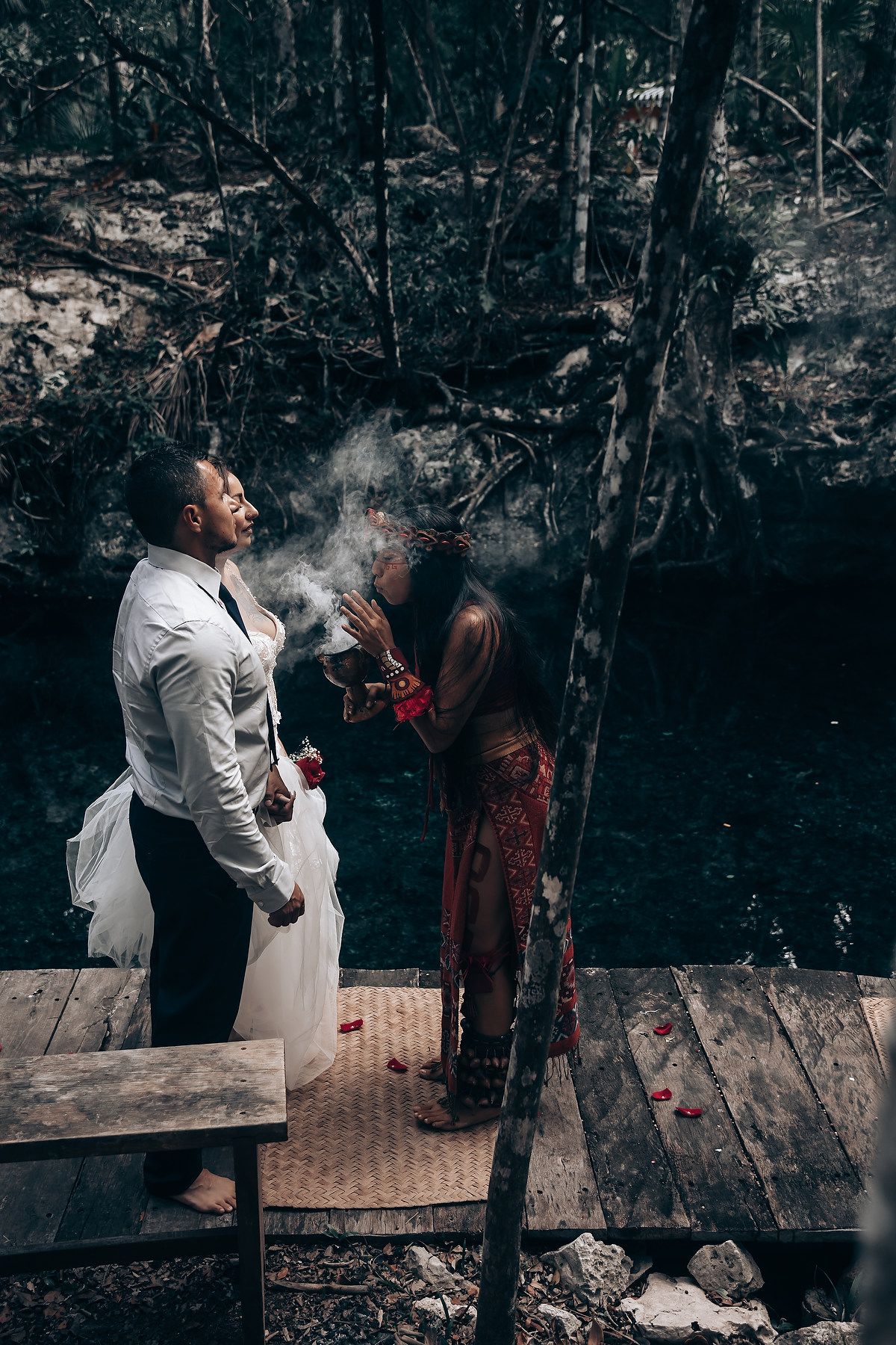 A wedding ceremony takes place in a rustic outdoor setting with dark moody lighting.