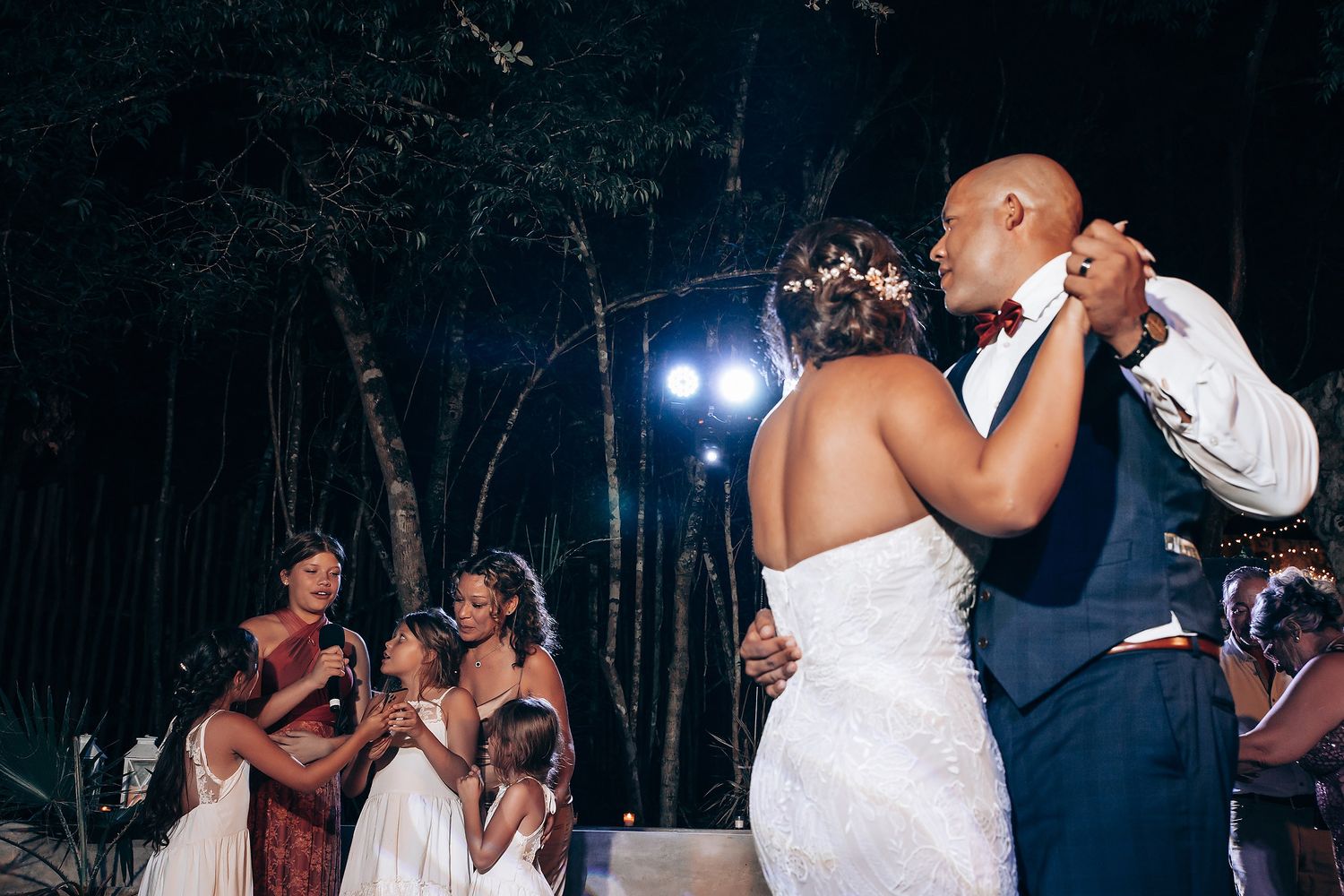 A couple shares their first dance at an outdoor evening wedding reception with guests watching in the background.