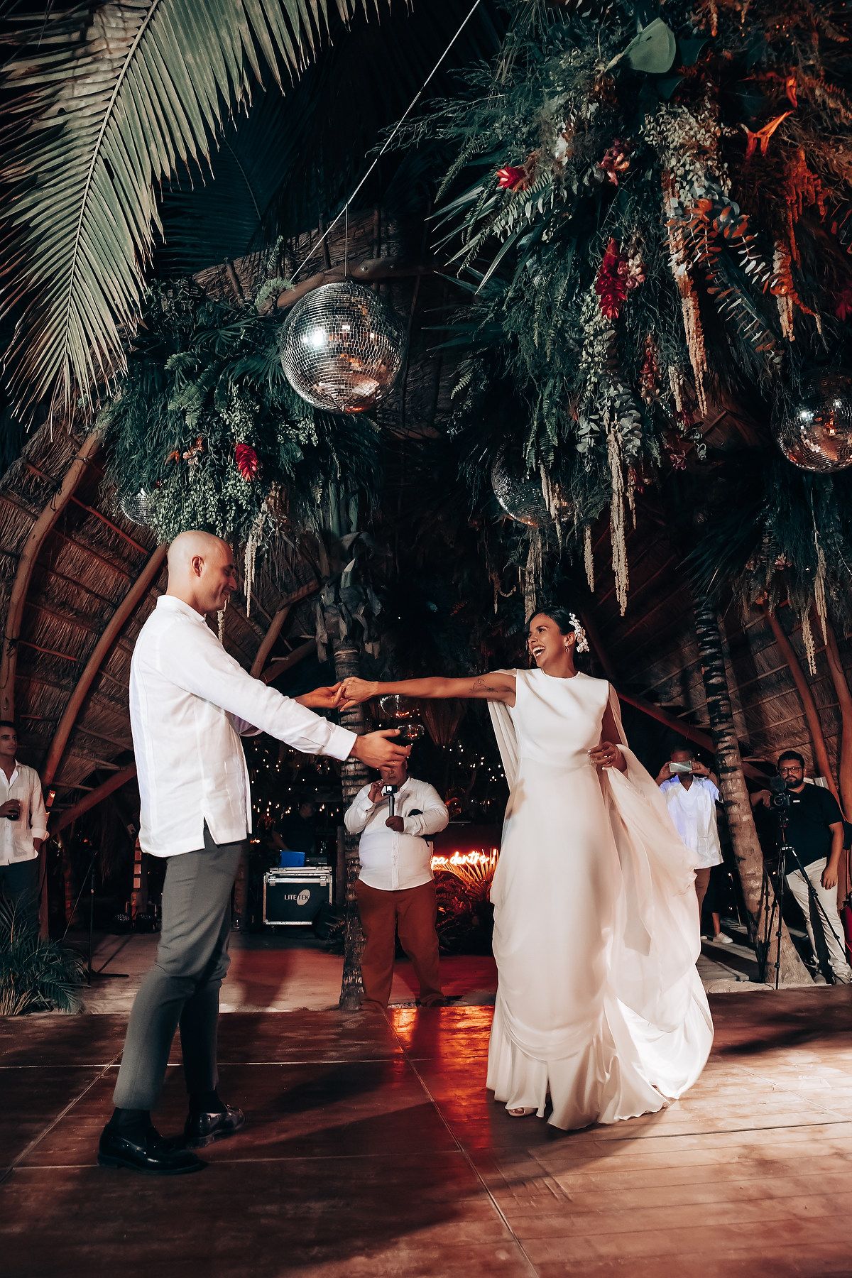 A couple shares a romantic dance sequence under palm trees and disco balls at a tropical wedding reception.