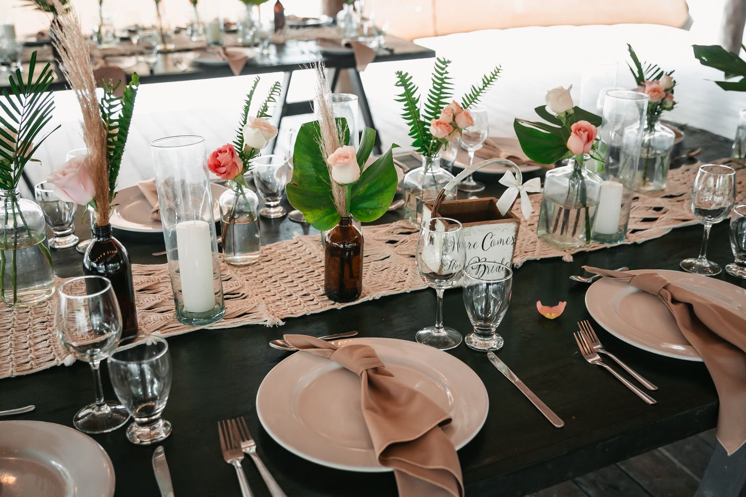 Elegant tropical wedding reception table with blush napkins, greenery centerpieces, and candles.