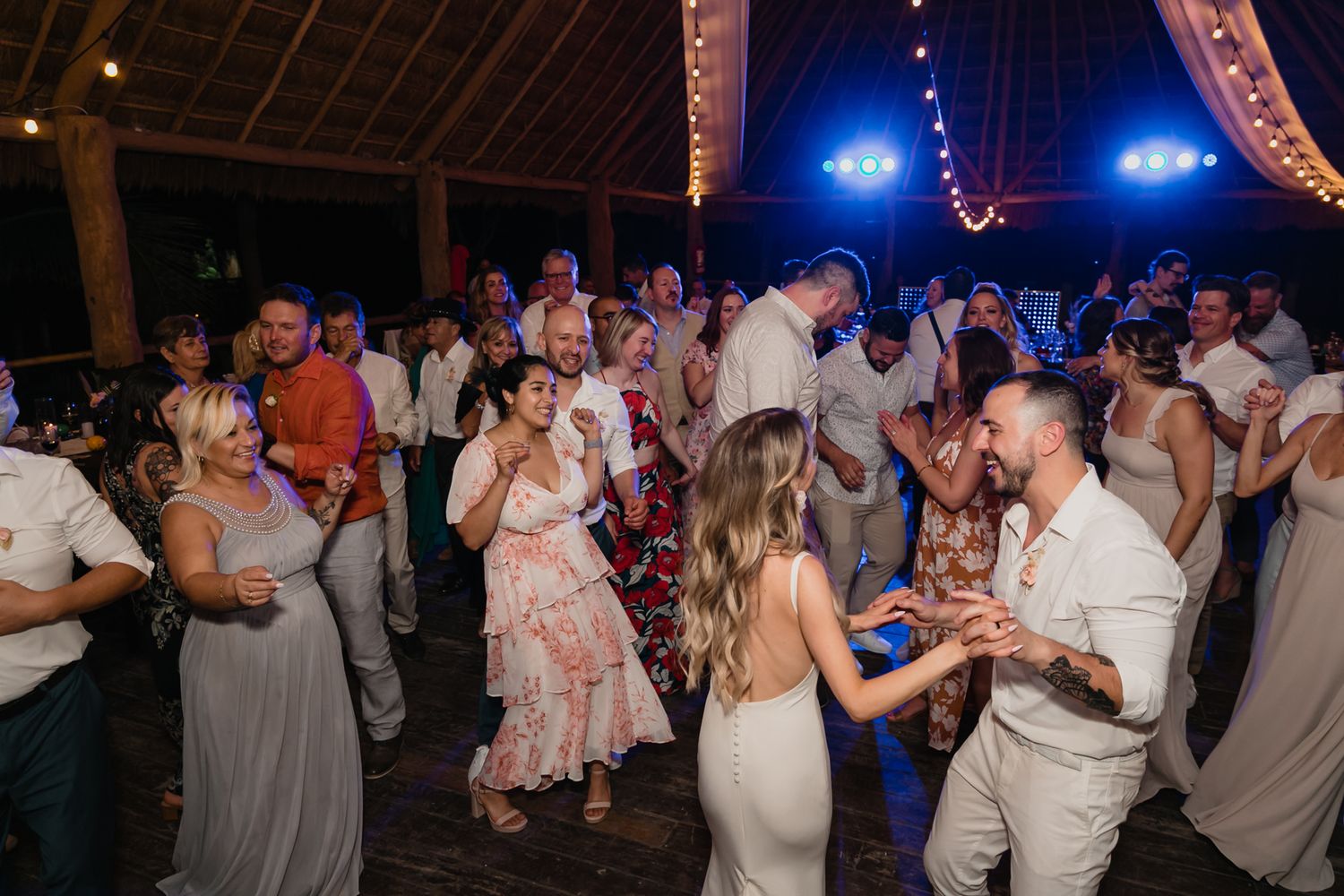 Bride and groom share a kiss on crowded dance floor during lively colorful wedding reception celebration.