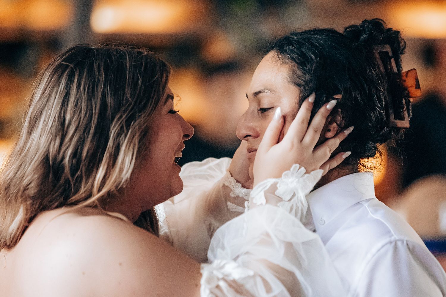 Two people share an intimate moment in white attire against a warm bokeh background.