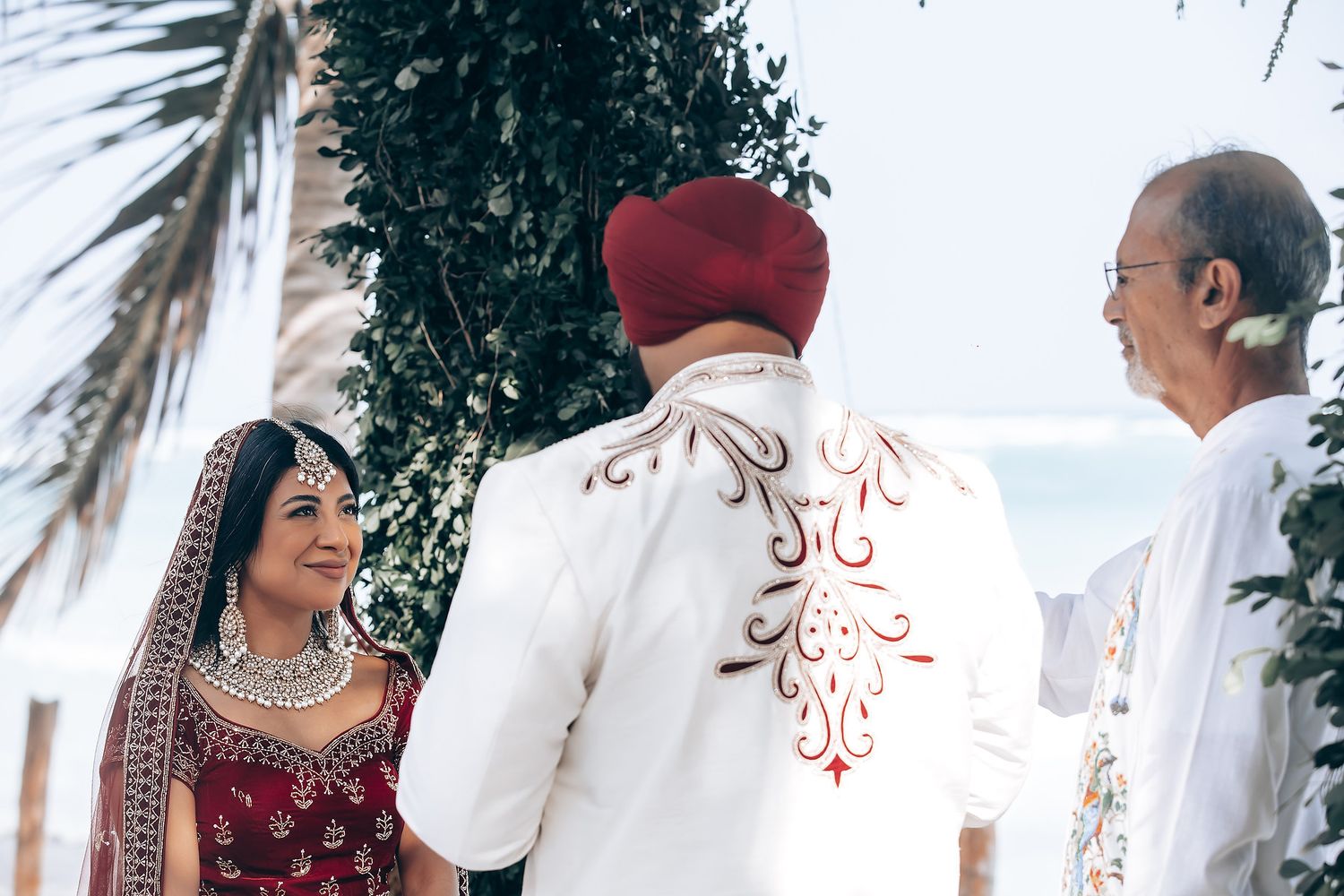 Beachfront Indian wedding ceremony with palm trees and floral arrangements.