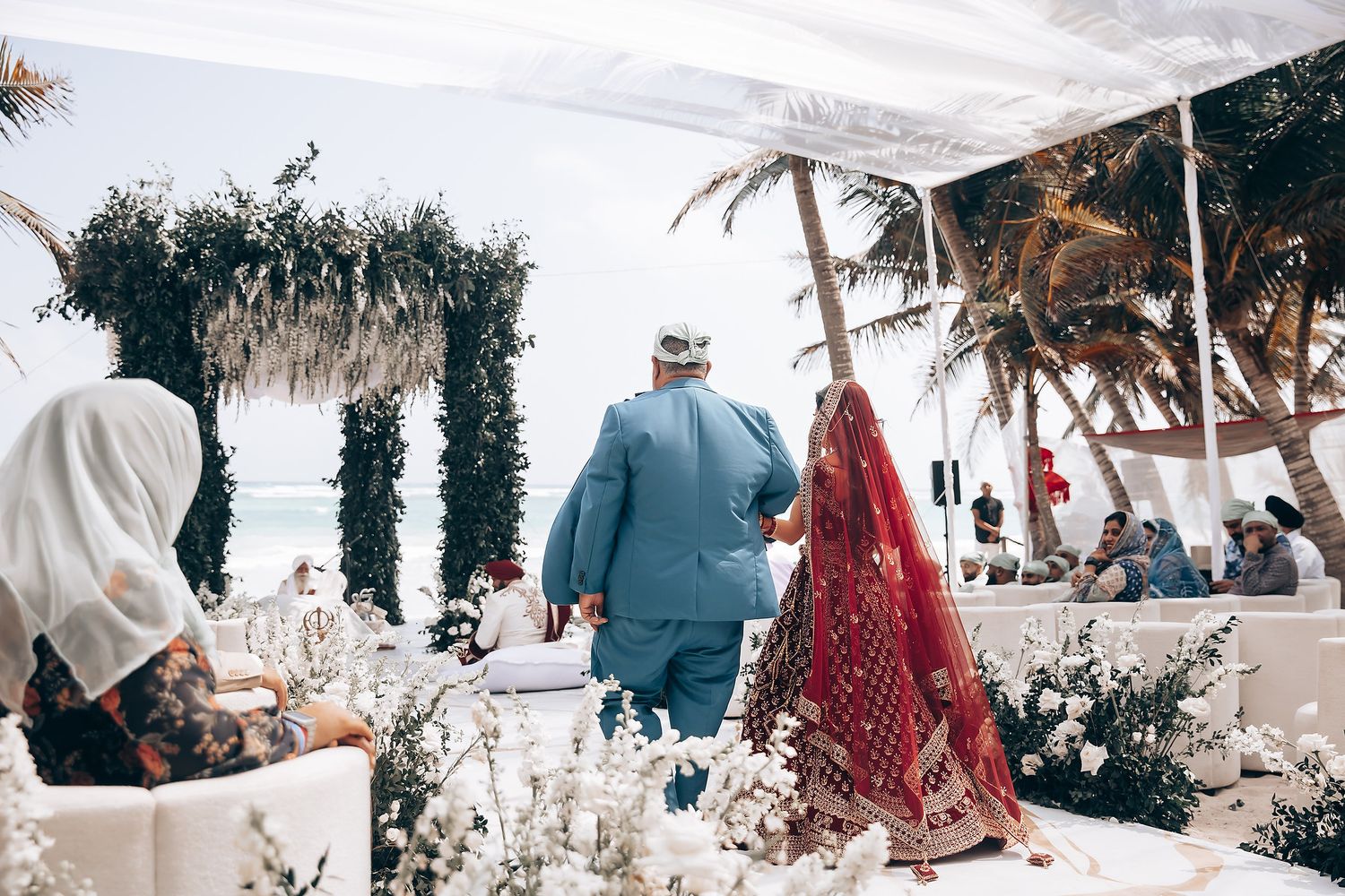 Outdoor beach wedding setup with white decor and palm trees in the background.