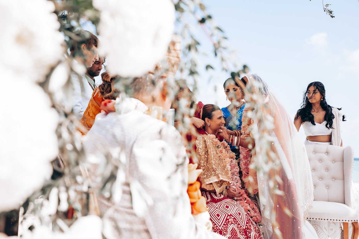 Guests celebrating at a beachfront wedding ceremony with white umbrellas and floral decorations.
