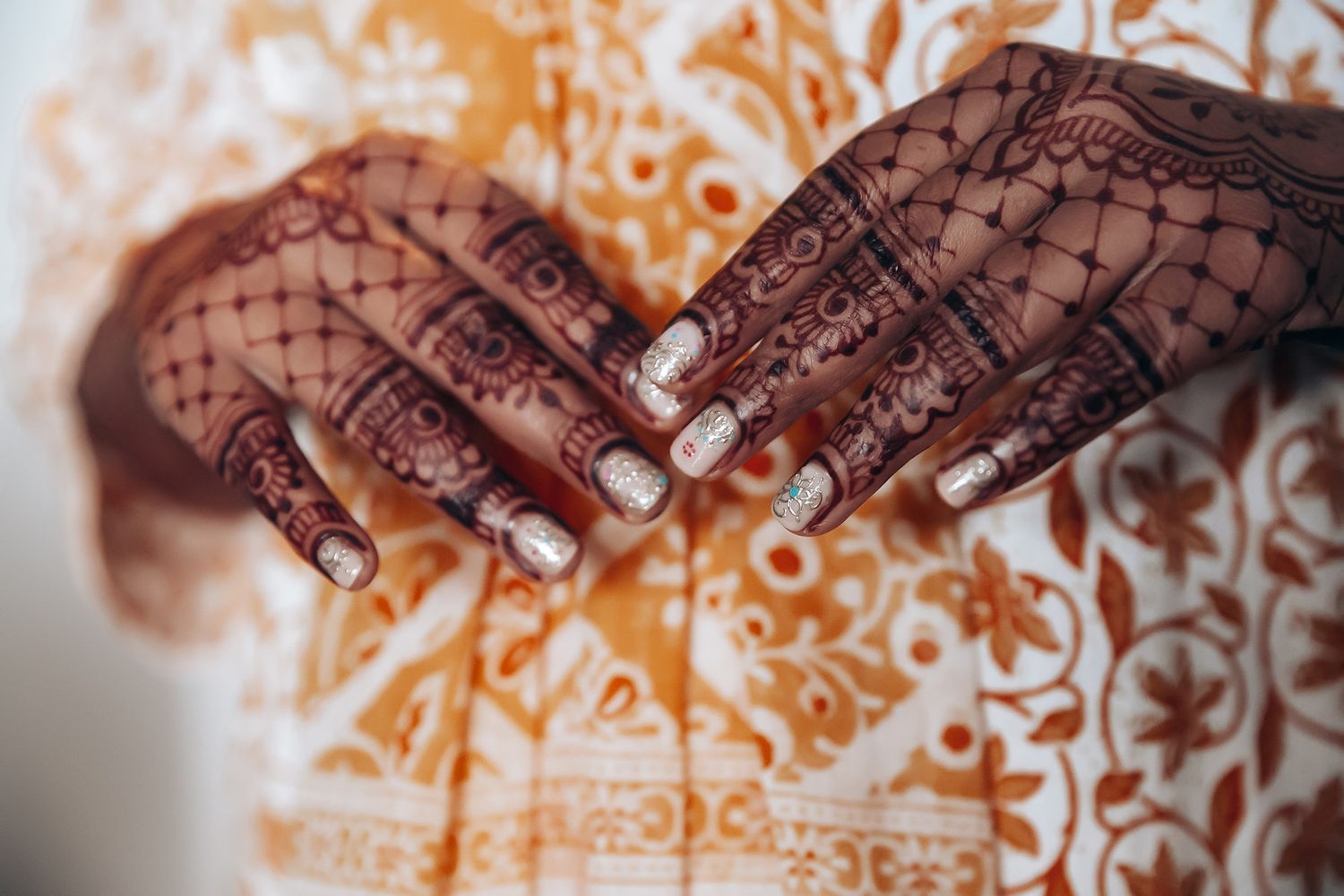 Detailed close-up of hands adorned with intricate henna designs against a patterned background.