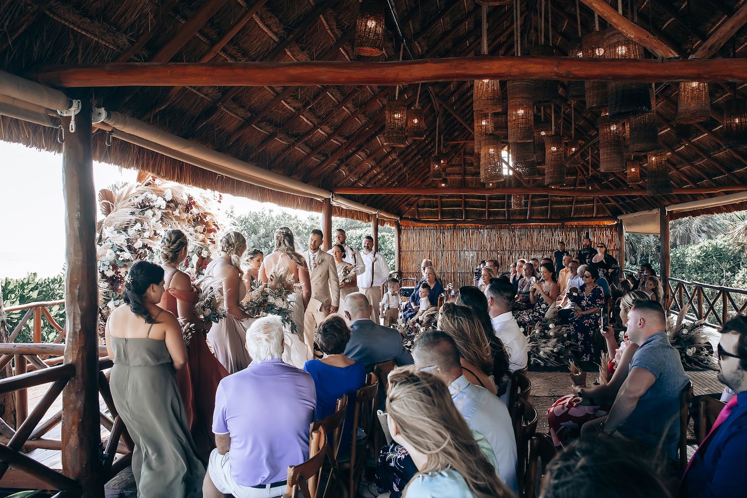 Wedding guests gathered in a covered outdoor venue overlooking tropical scenery.