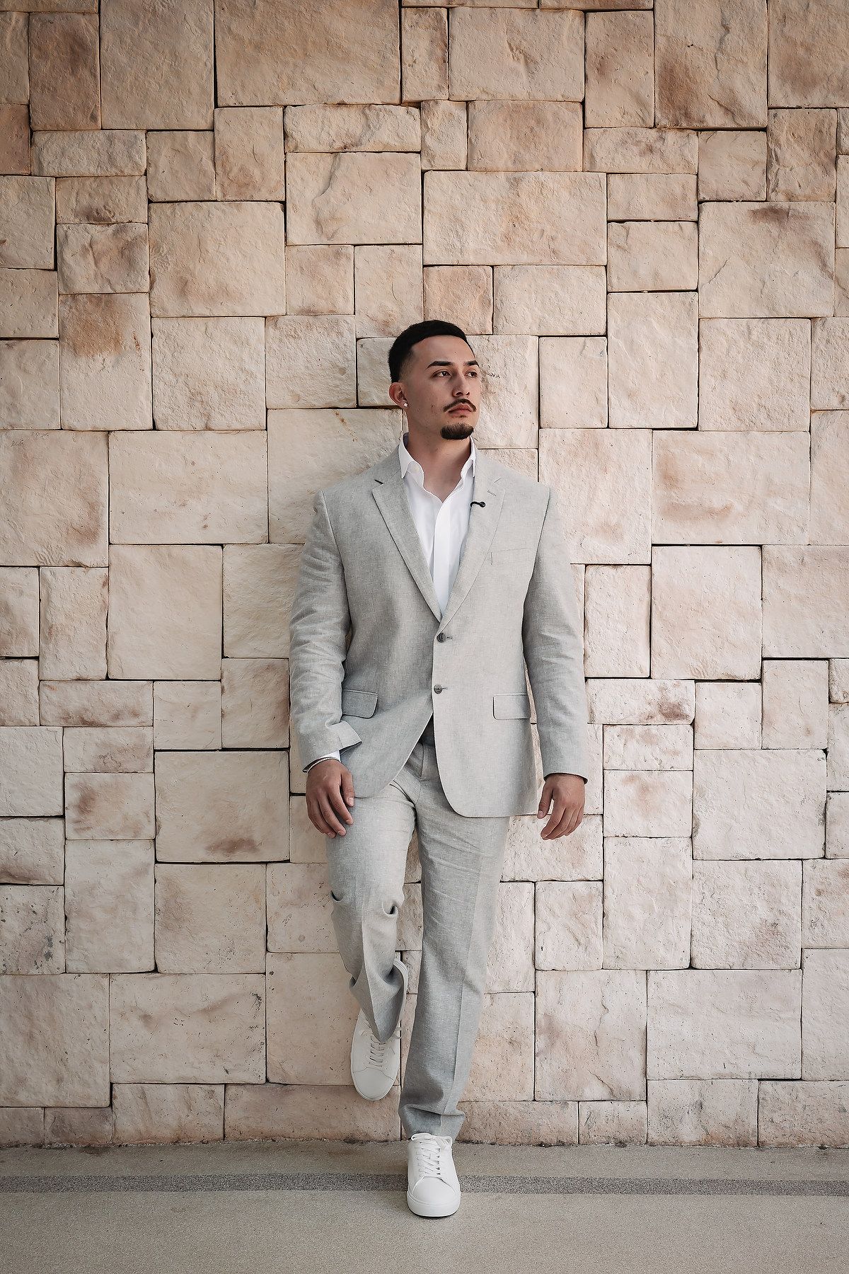 A sequence of playful poses in a light gray suit against a textured stone wall background.
