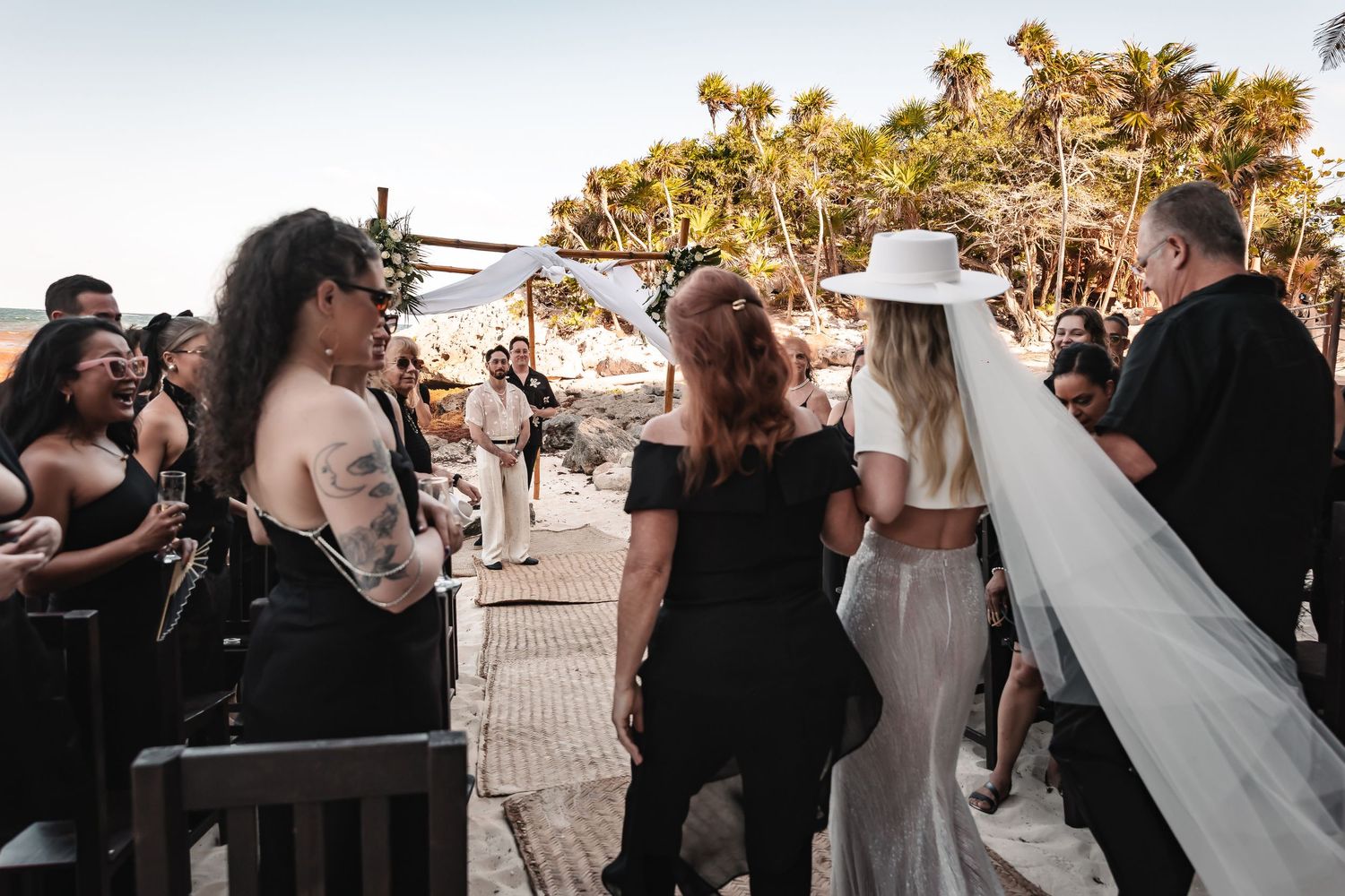Wedding celebration on beach with guests gathering under golden evening light.