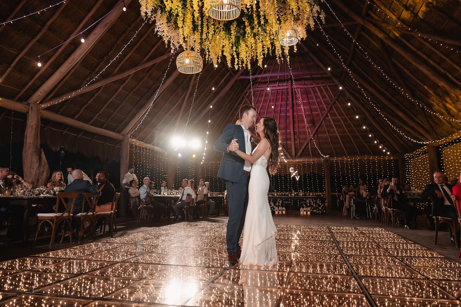 Newlyweds share their first dance under yellow floral installations in a rustic barn venue.