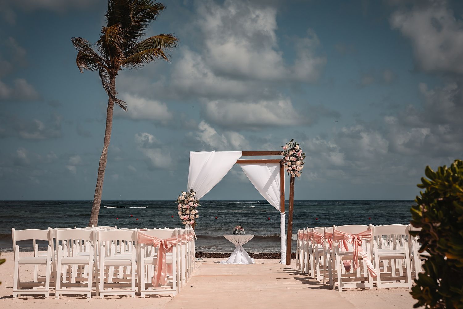 Beach wedding ceremony setup with white chairs and floral arch overlooking the ocean.