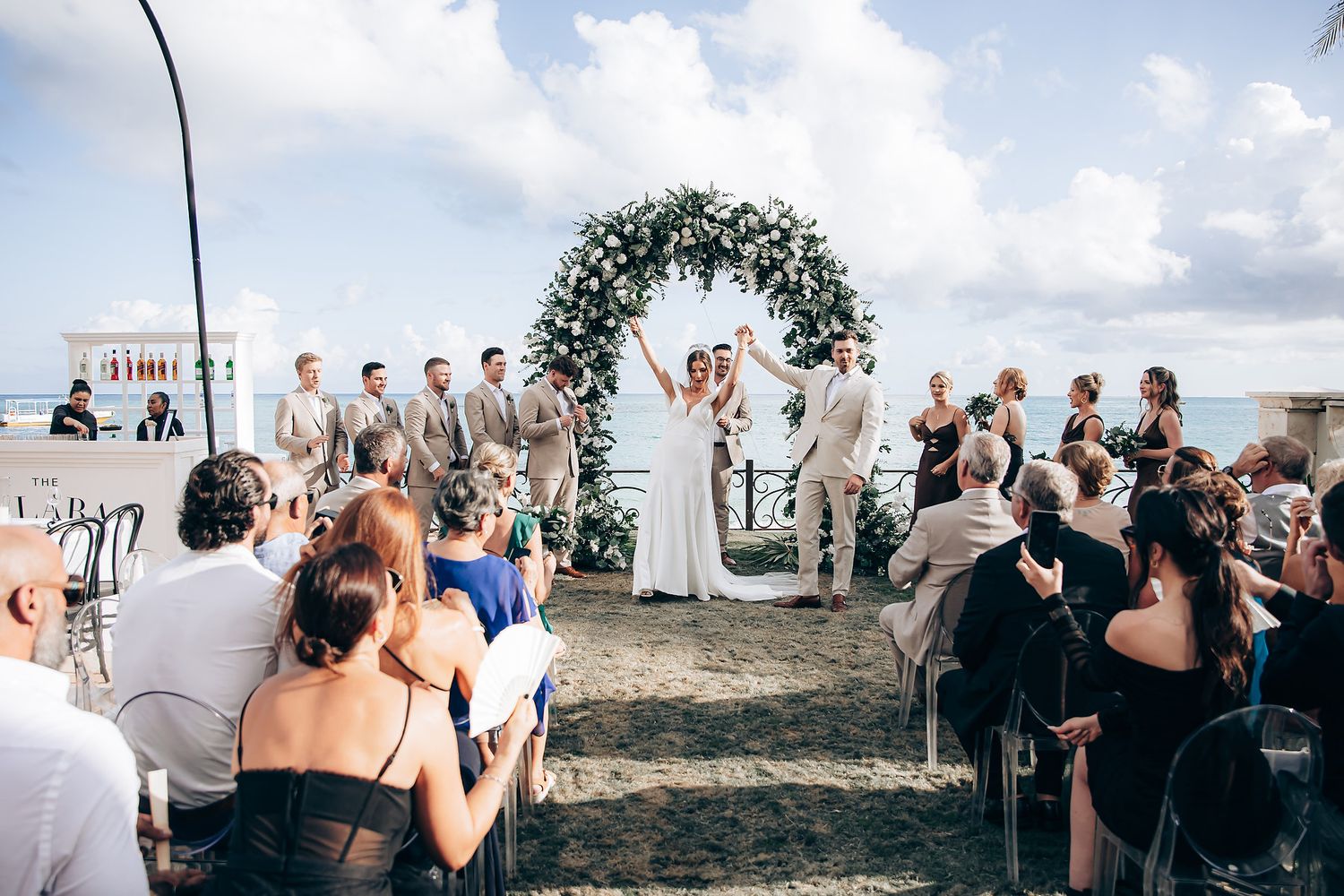 Wedding guests celebrate during an outdoor reception with ocean views.