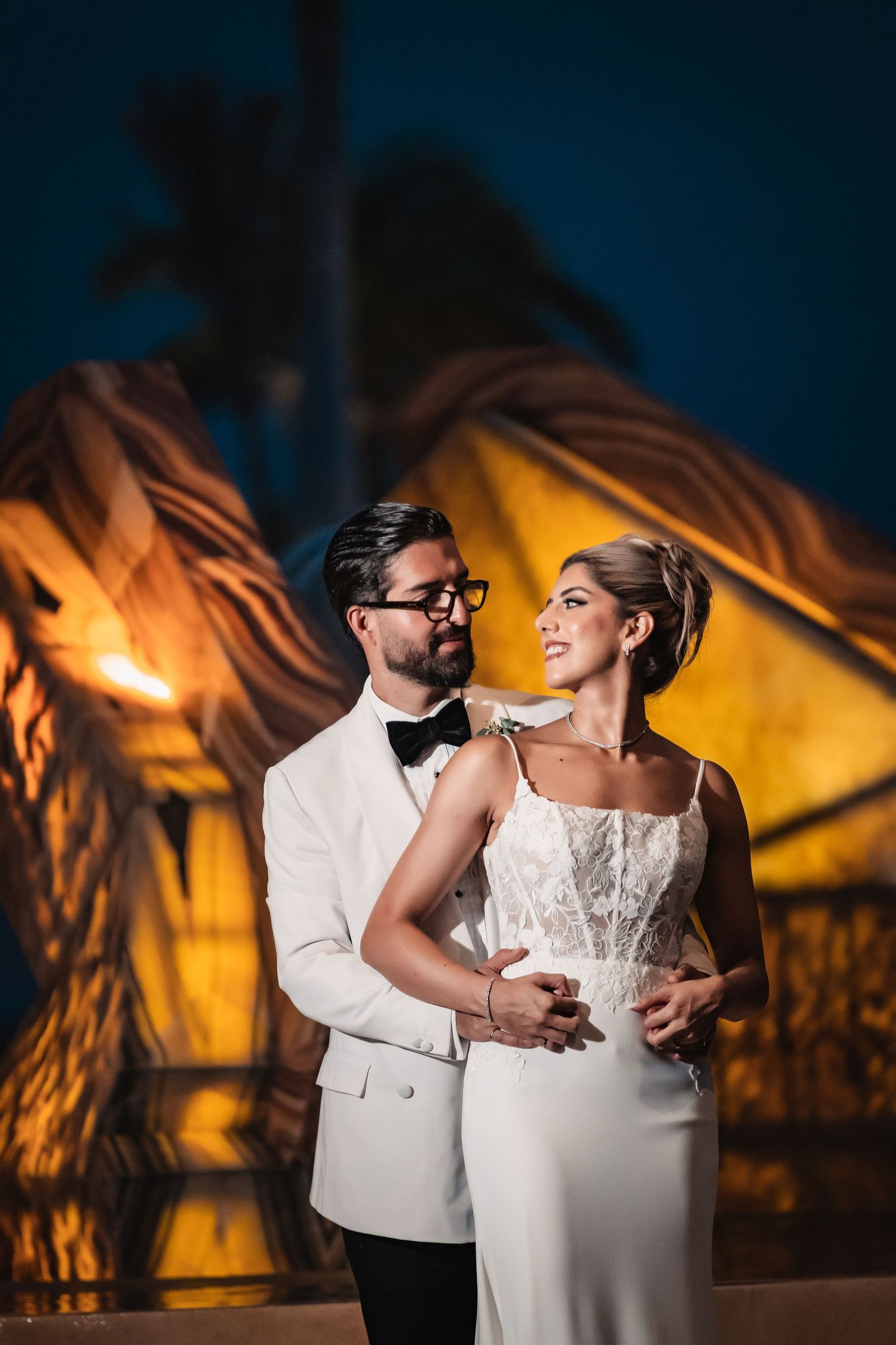 Wedding couple dancing in dramatic lighting against warm amber background.