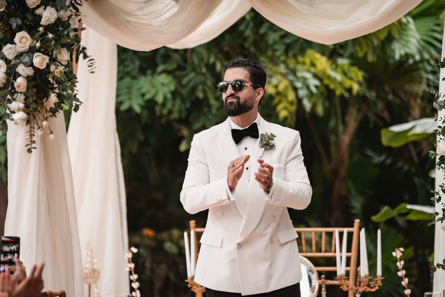 Wedding ceremony space with white fabric draping and tropical garden backdrop.