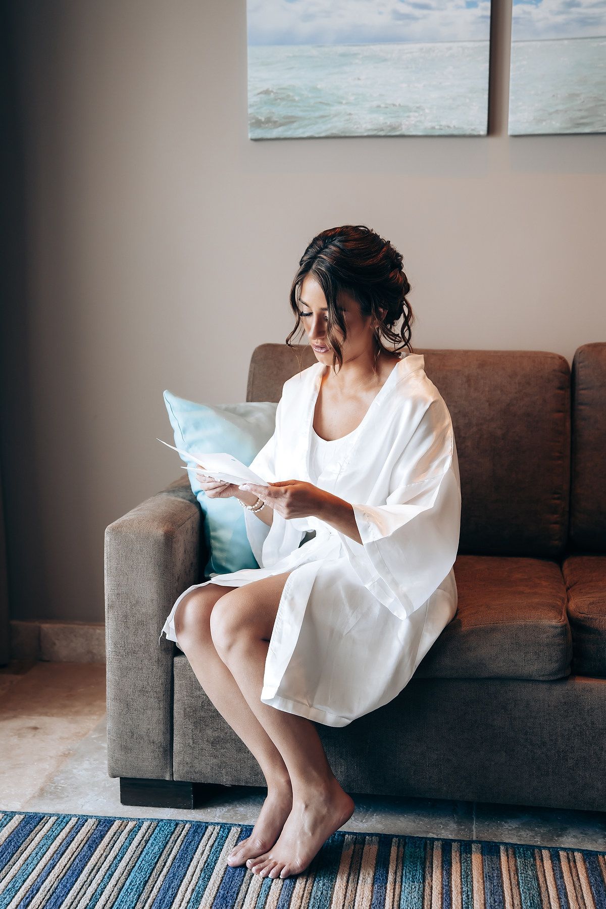 Artistic photo series showing relaxed poses on a gray couch with coastal artwork in the background.