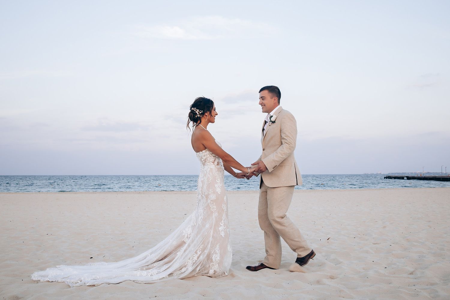 Romantic beach wedding scene with couple in white dress and tan suit against ocean backdrop.