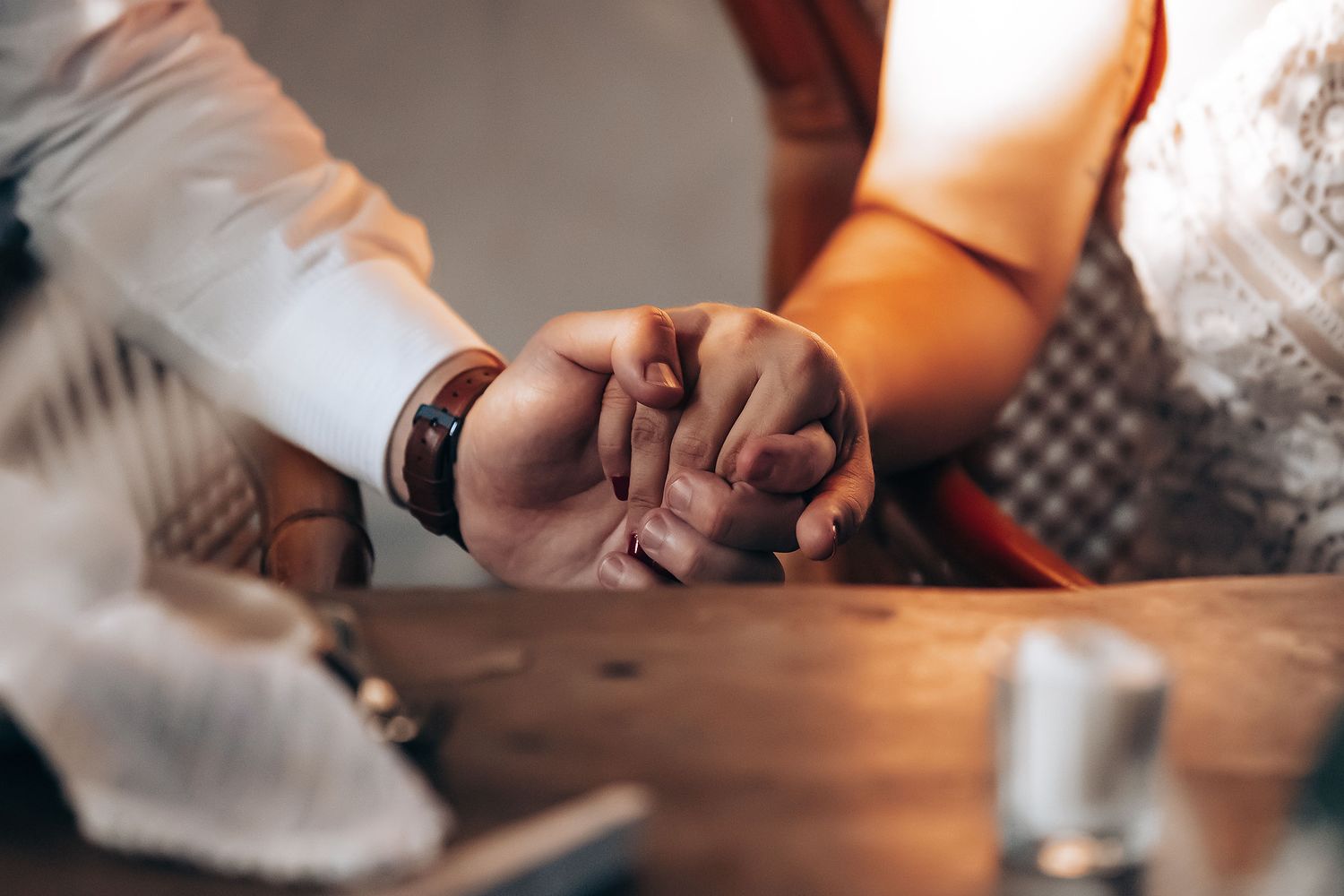 Two hands holding each other in a comforting gesture across a wooden table.
