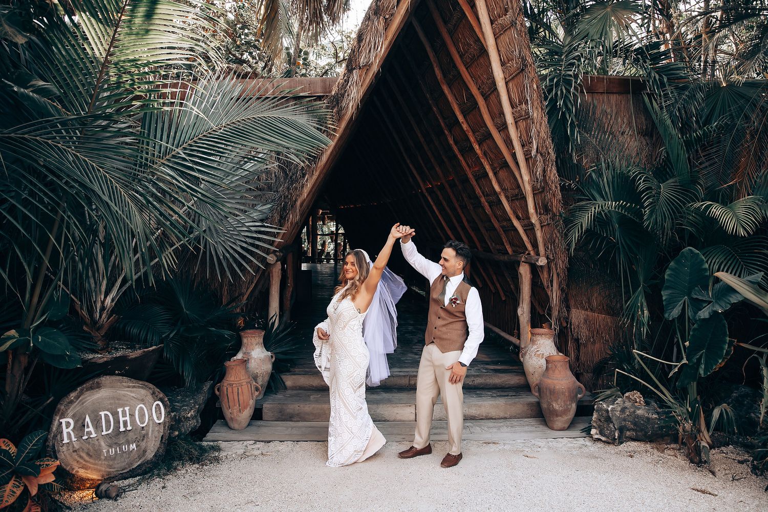 Wedding couple walking through a rustic wooden archway decorated with dried pampas grass and palm fronds.