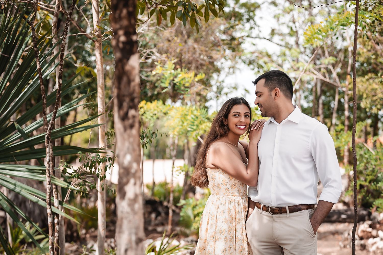 Couple shares joyful moments along tree-lined garden path with filtered sunlight.