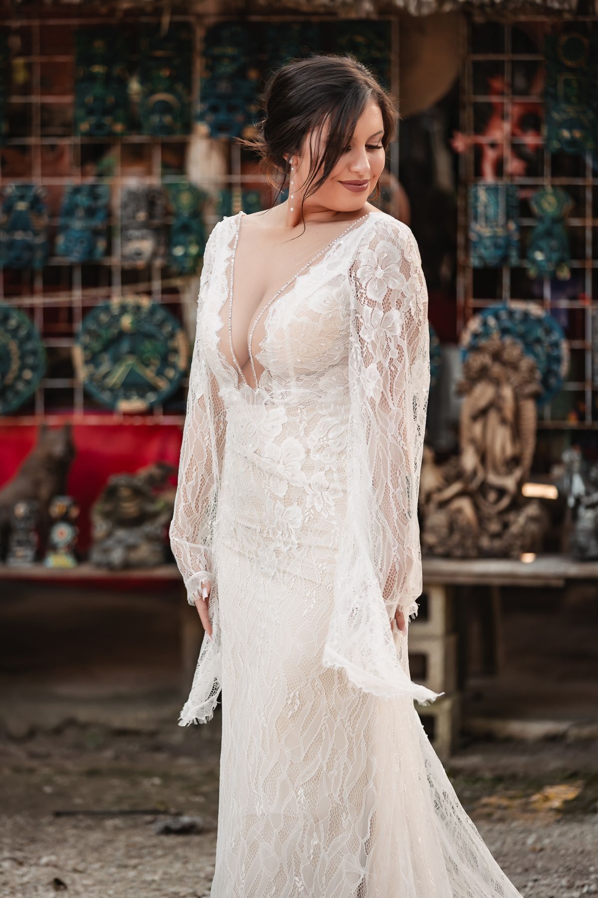 A bride in a flowing lace wedding gown with long sleeves poses against a colorful backdrop.