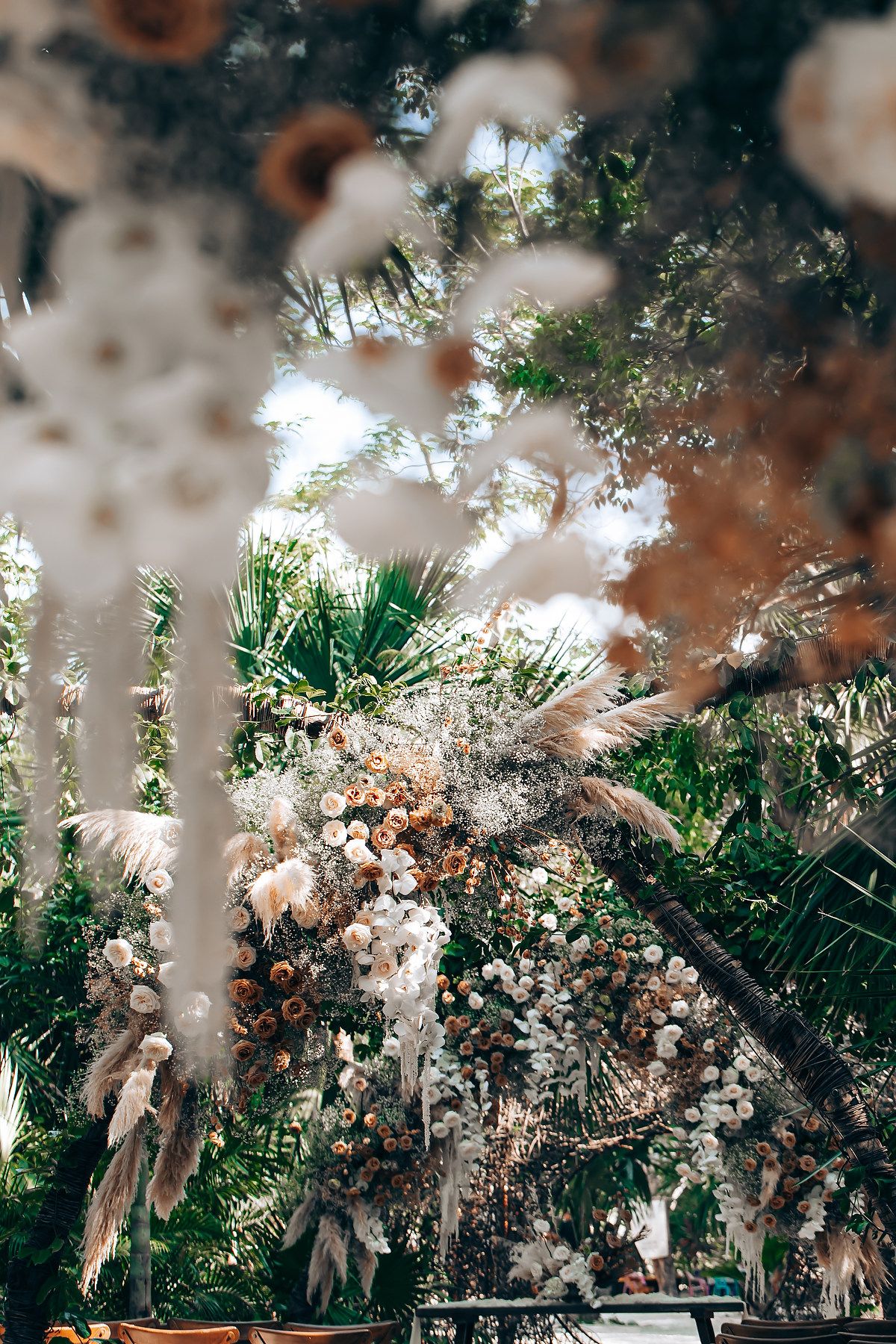 Delicate white pampas grass and tropical palm fronds create a dreamy, ethereal outdoor garden scene in soft focus.