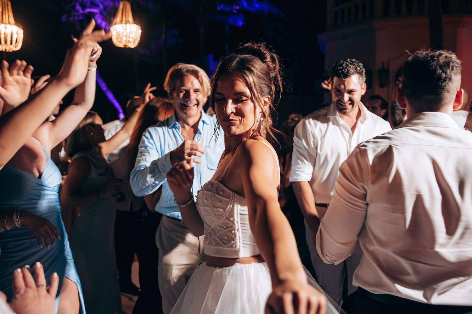 People dancing and celebrating at a wedding reception with colorful lighting and festive atmosphere.