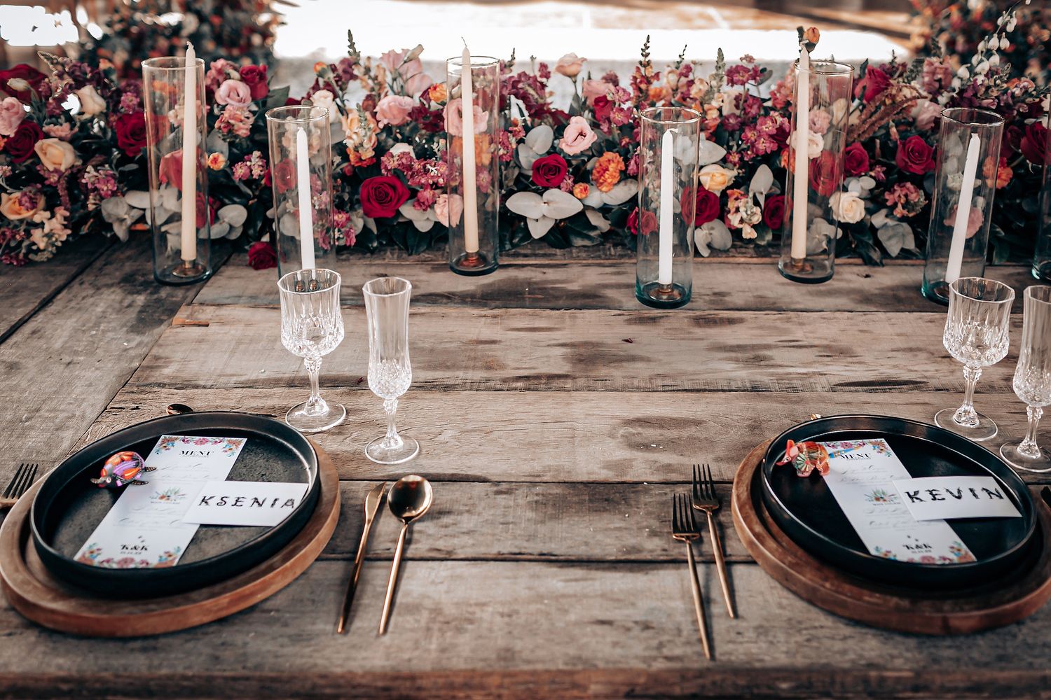 Elegant place settings with wine glasses and rustic charger plates arranged on a wooden table at a wedding reception.
