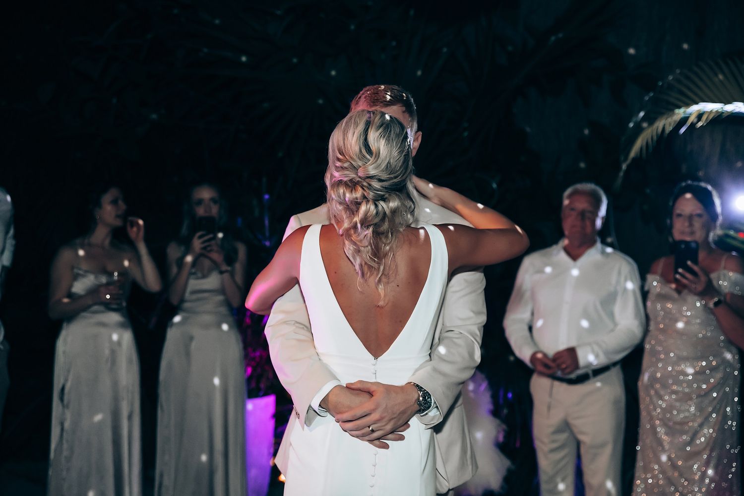 A backlit wedding reception scene with guests watching a special moment on the dance floor.