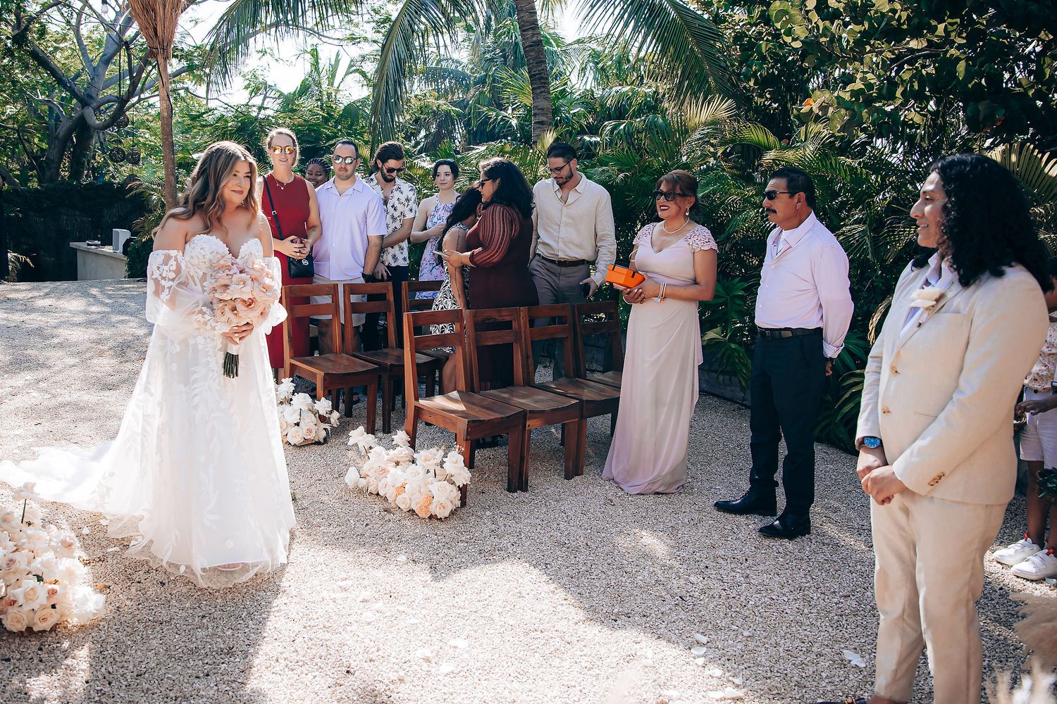 Wedding guests gather outdoors under palm trees for a tropical celebration.