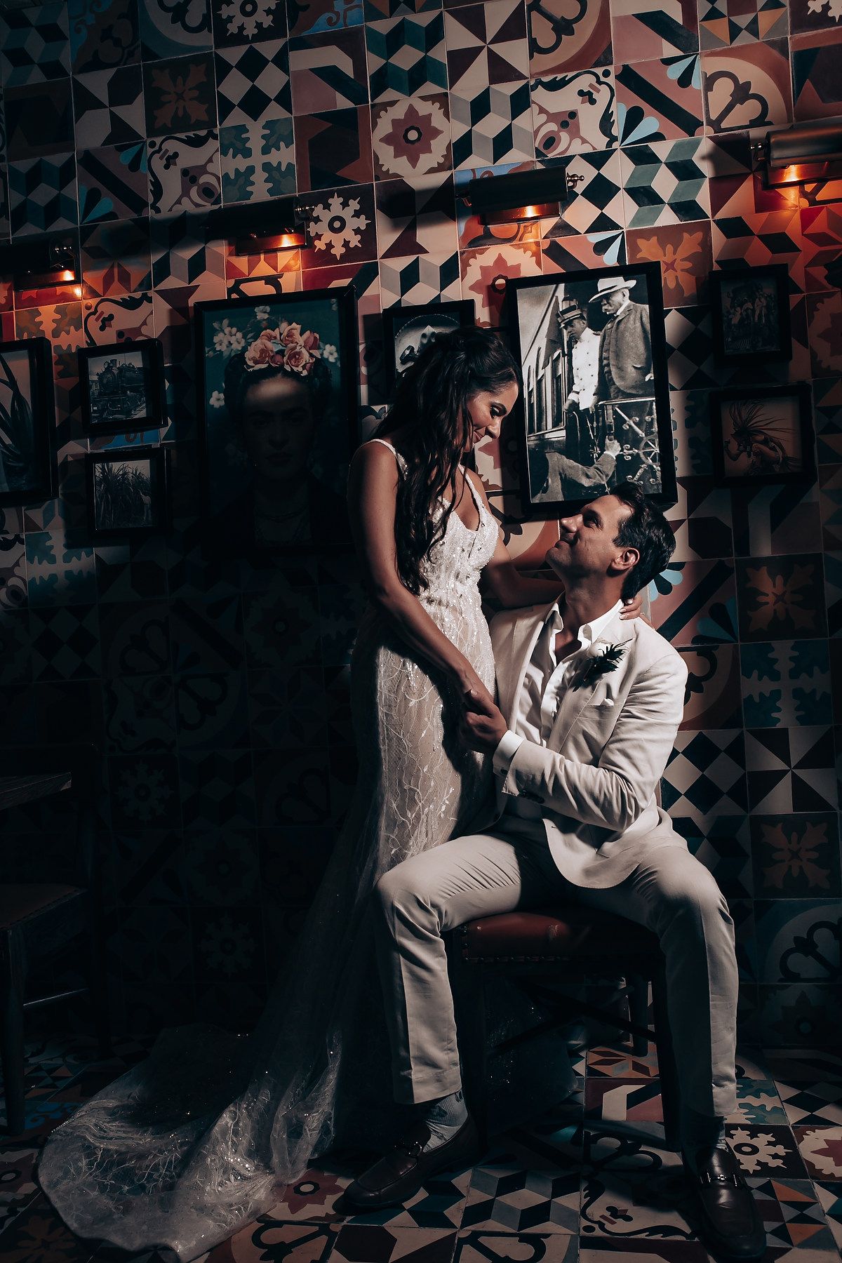 Dramatic wedding photo against patterned tile wall with moody lighting and vintage decor.