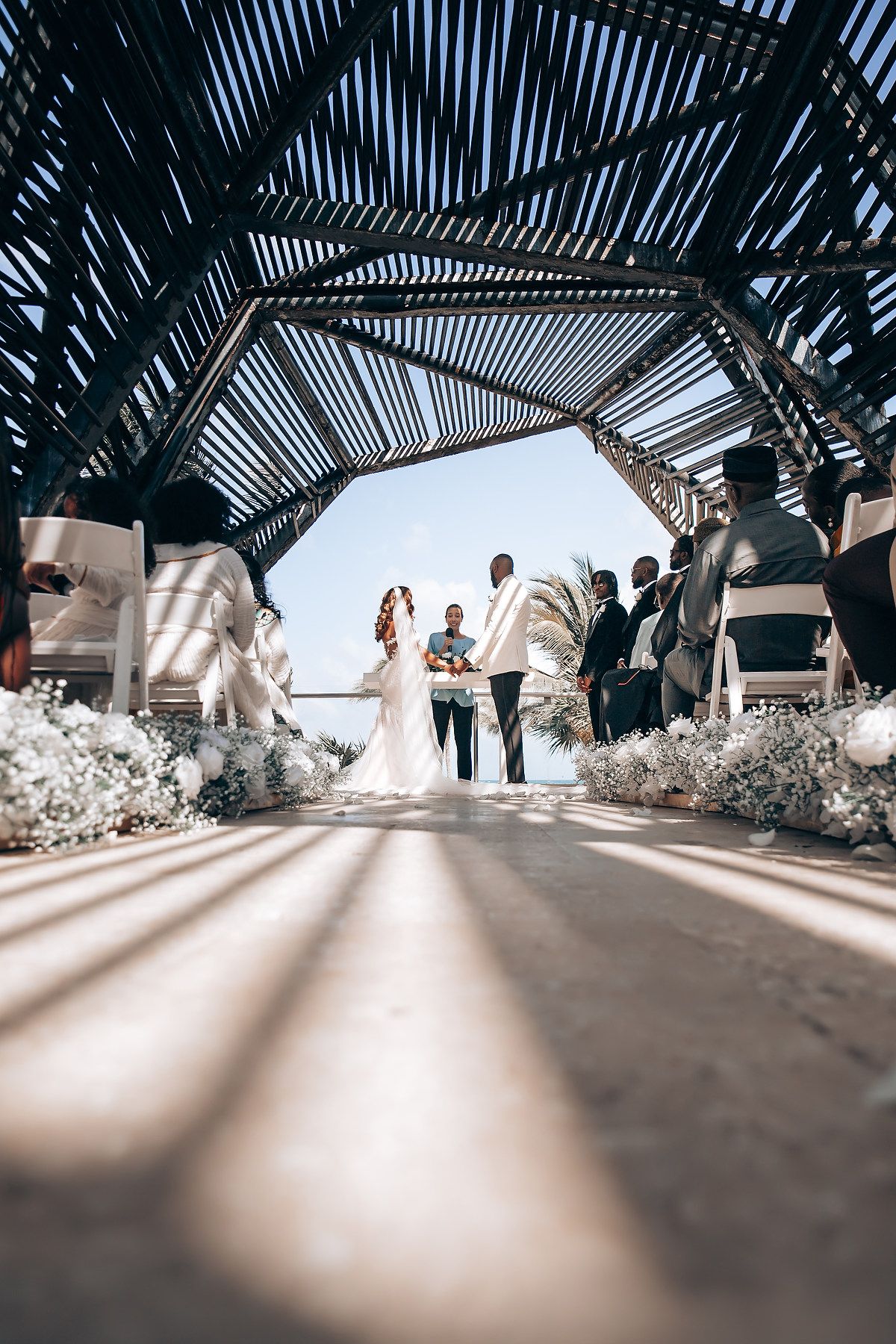 Low-angle view of a wedding ceremony under a modern pergola with geometric shadows.