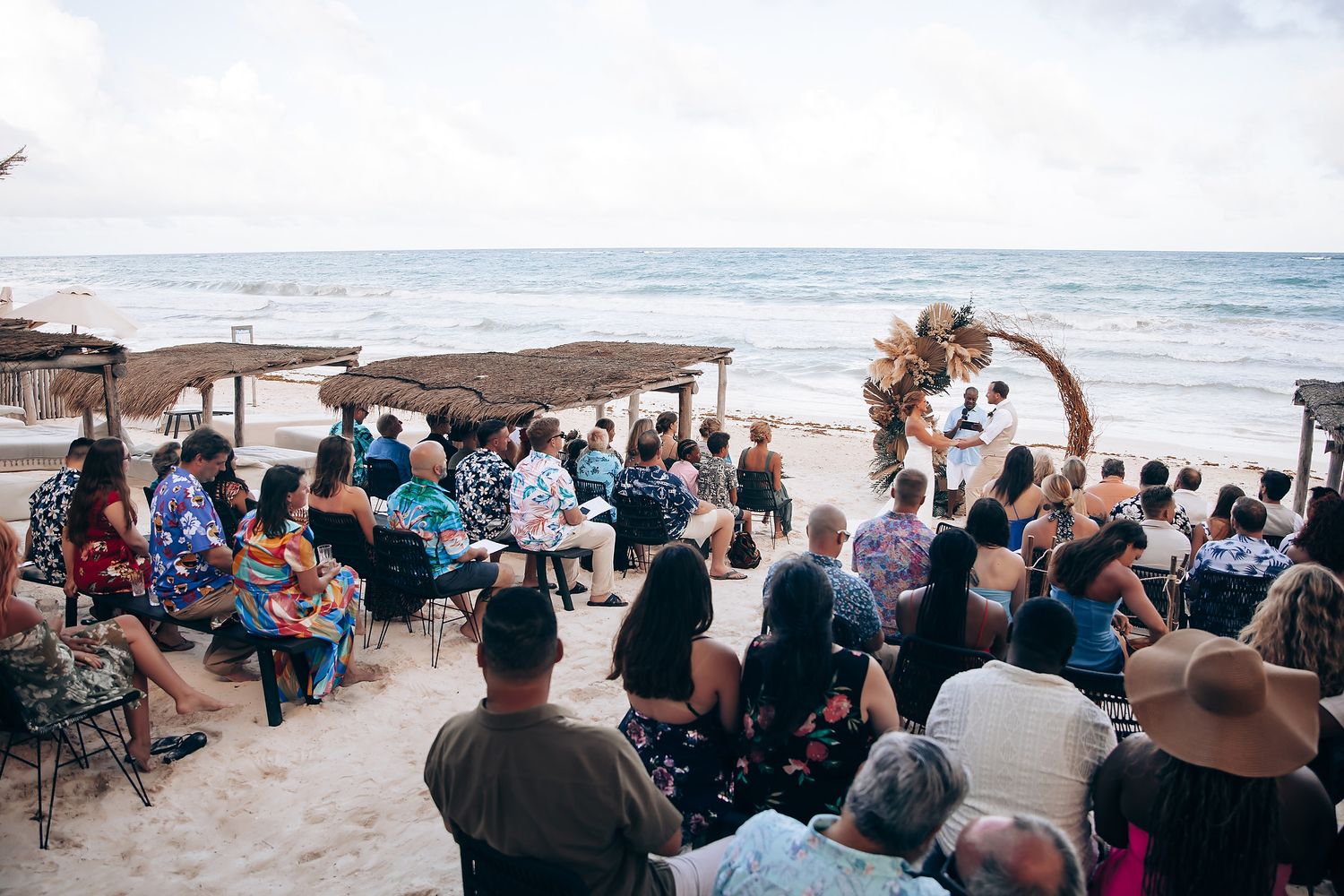 Panoramic view of beach wedding guests seated on chairs facing the ocean.