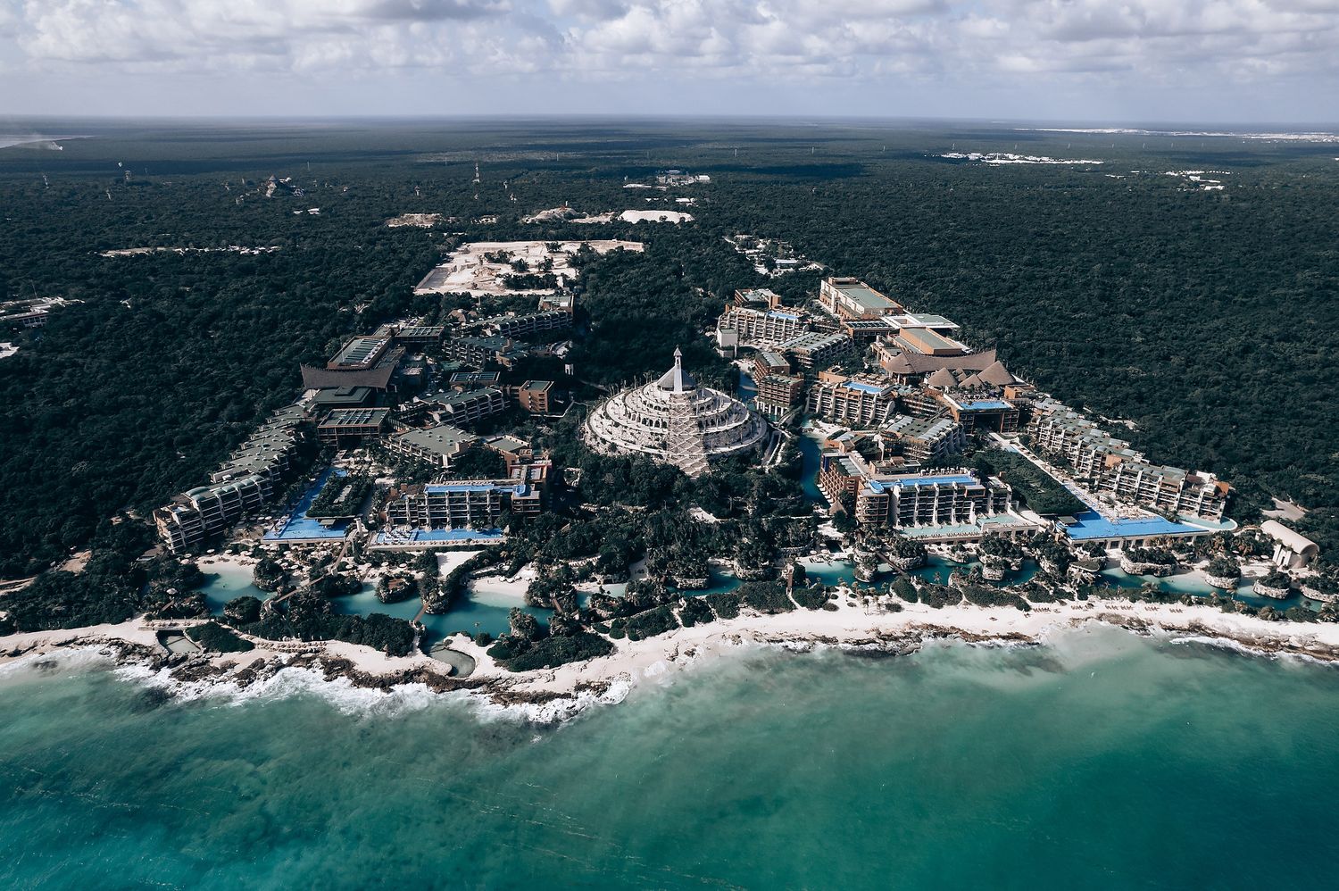 Aerial panoramic view of a rocky coastline with luxury resorts and buildings nestled along turquoise Caribbean waters.