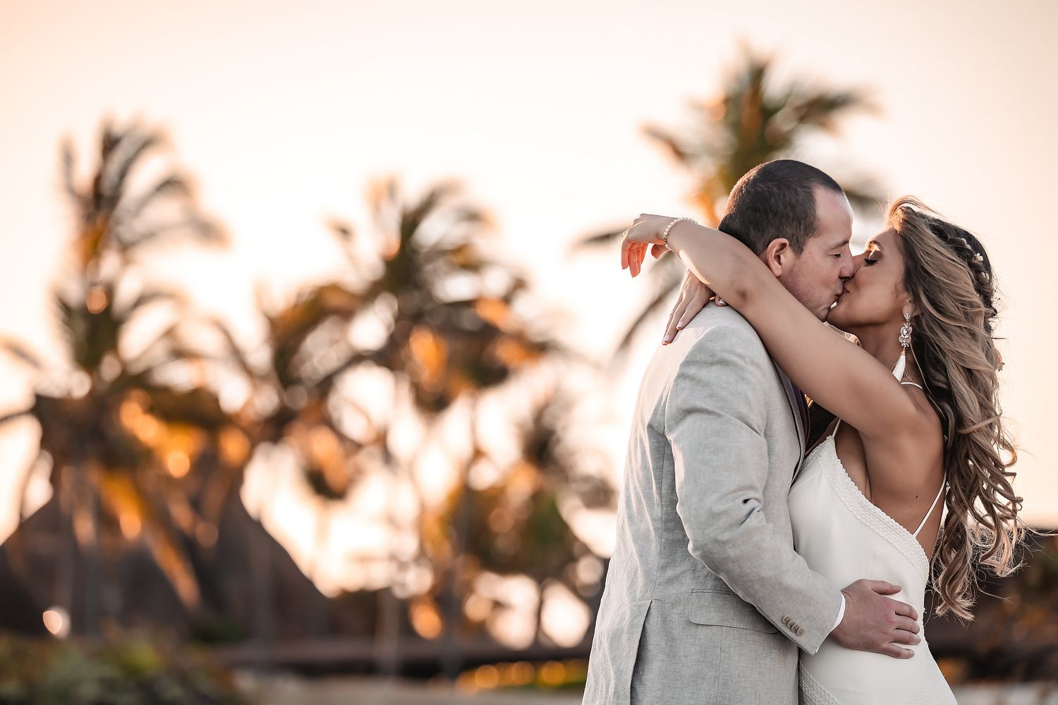 A romantic sunset moment captured among palm trees at a beach wedding.