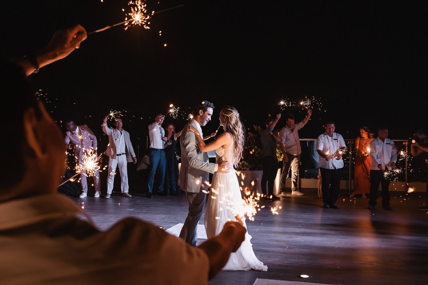 Sparklers illuminate a nighttime wedding celebration as couple dances surrounded by guests.