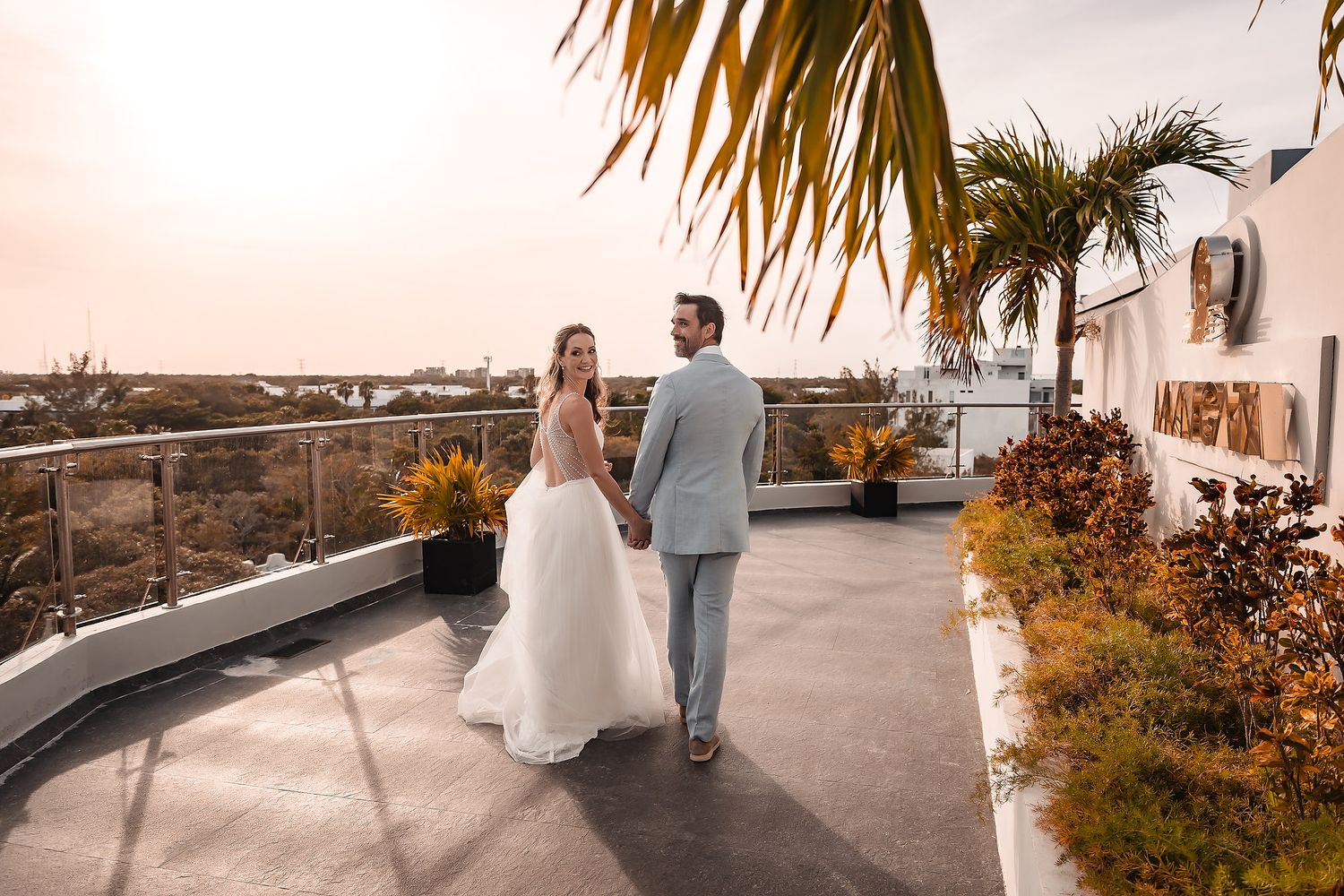 Sunset wedding portrait on tropical terrace with palm trees and ocean view.