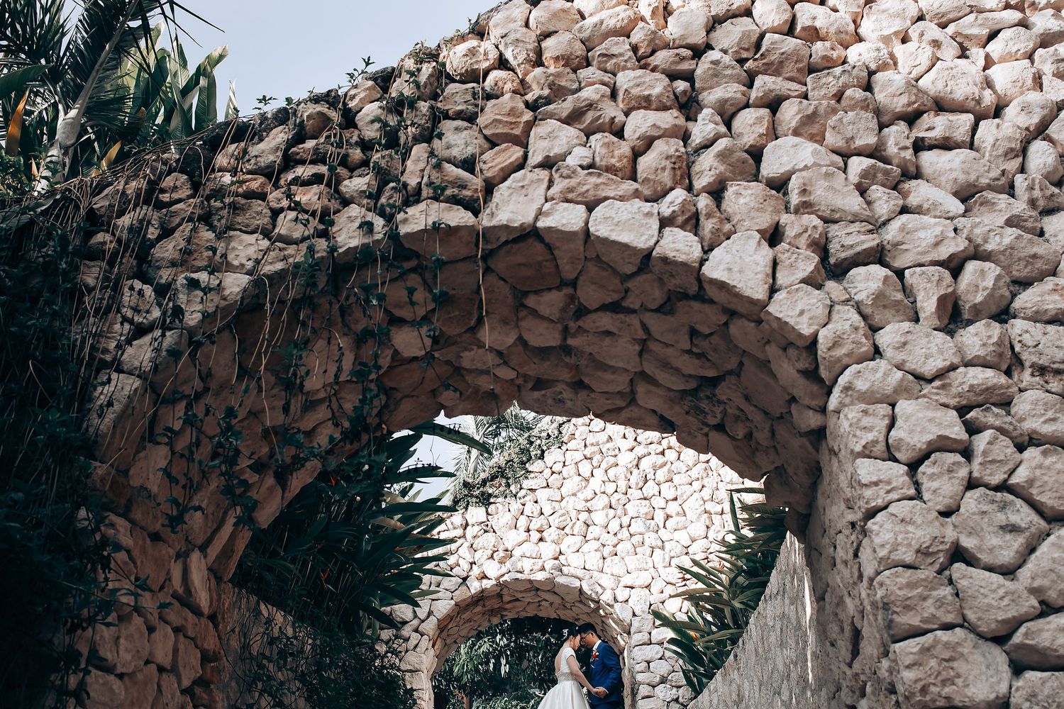 Stone archways line a scenic coastal path with tropical foliage and ocean views.