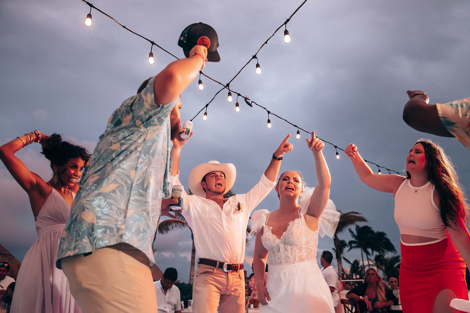 Wedding guests dance and celebrate under string lights at dusk.