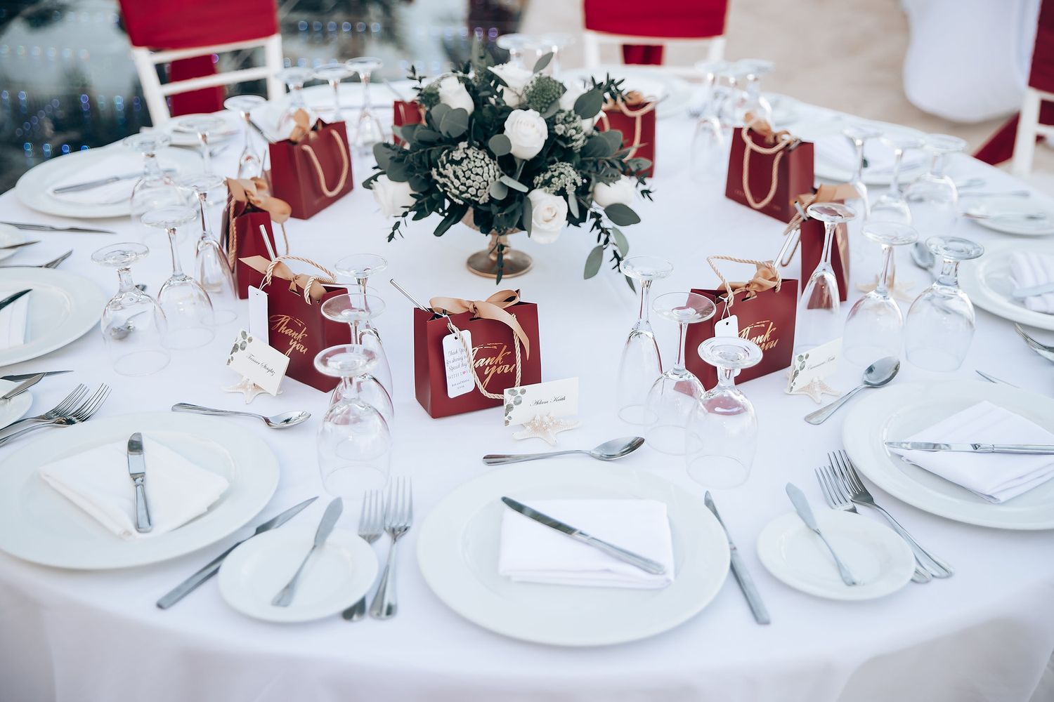 Elegant wedding reception table setting with burgundy and white decor and floral centerpieces.