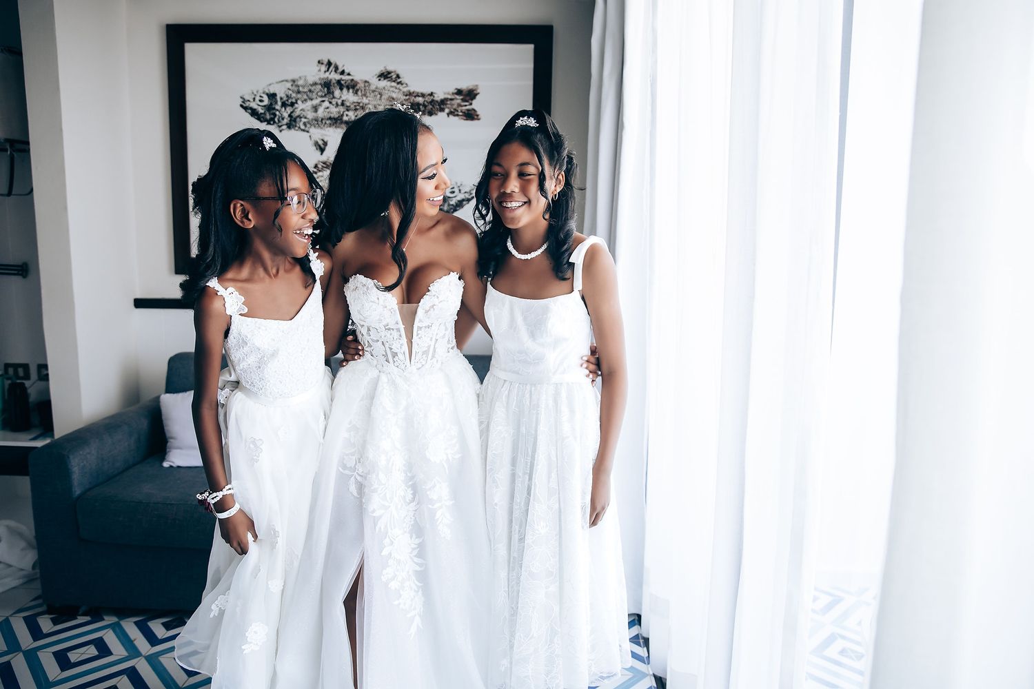 Bridesmaids in white dresses pose together against light curtain background.