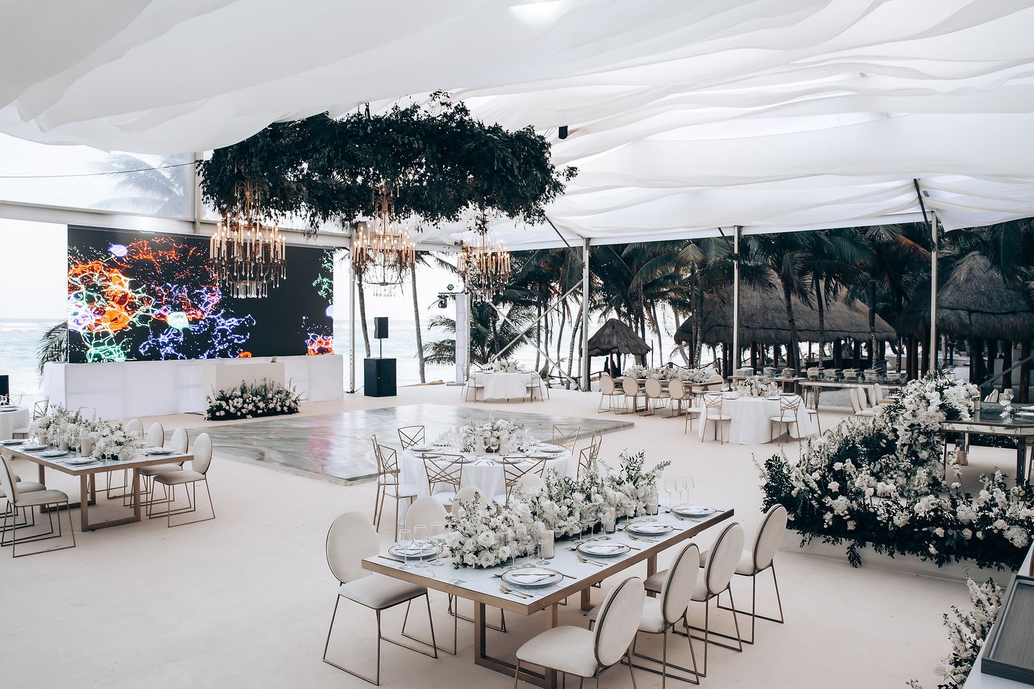 Modern wedding reception venue decorated with white floral arrangements and geometric furniture.