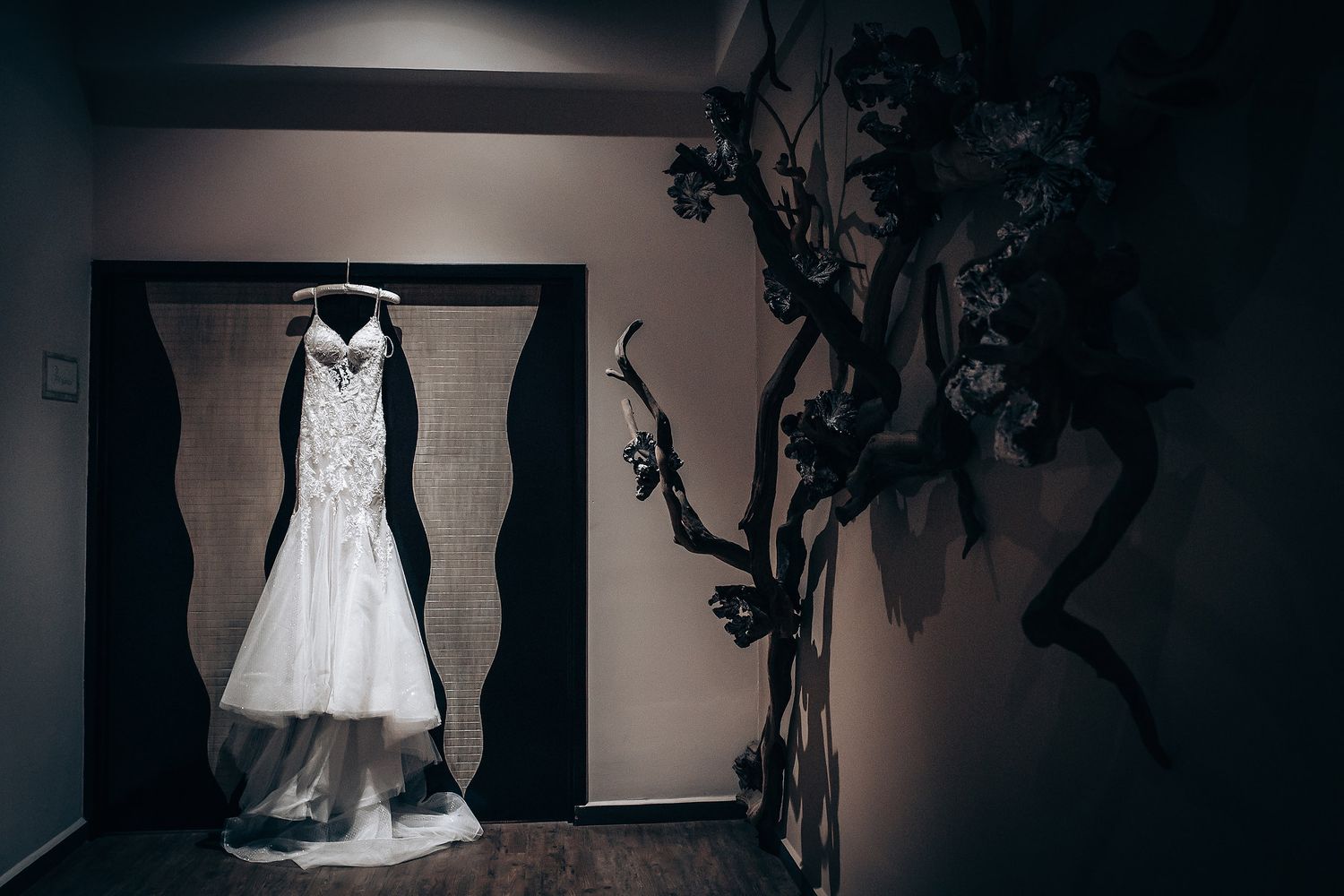 A collection of wedding dresses and formal gowns displayed on hangers in a dimly lit room.