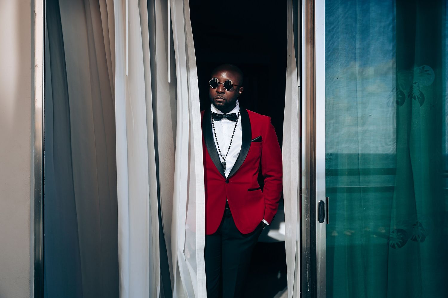 Person in red blazer and black shirt poses against a teal and white background in an artistic portrait series.