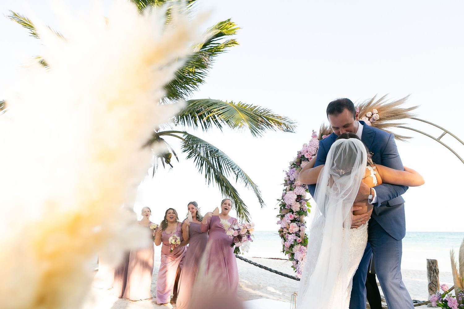 Romantic beach wedding scene with palm fronds and soft golden lighting at sunset.