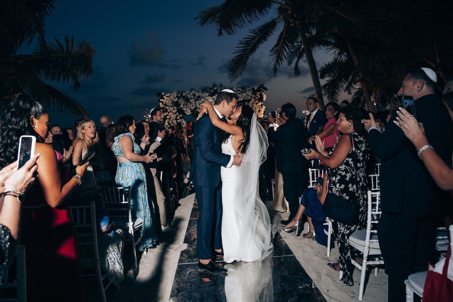 Wedding couple sharing first dance surrounded by guests at beachside reception.